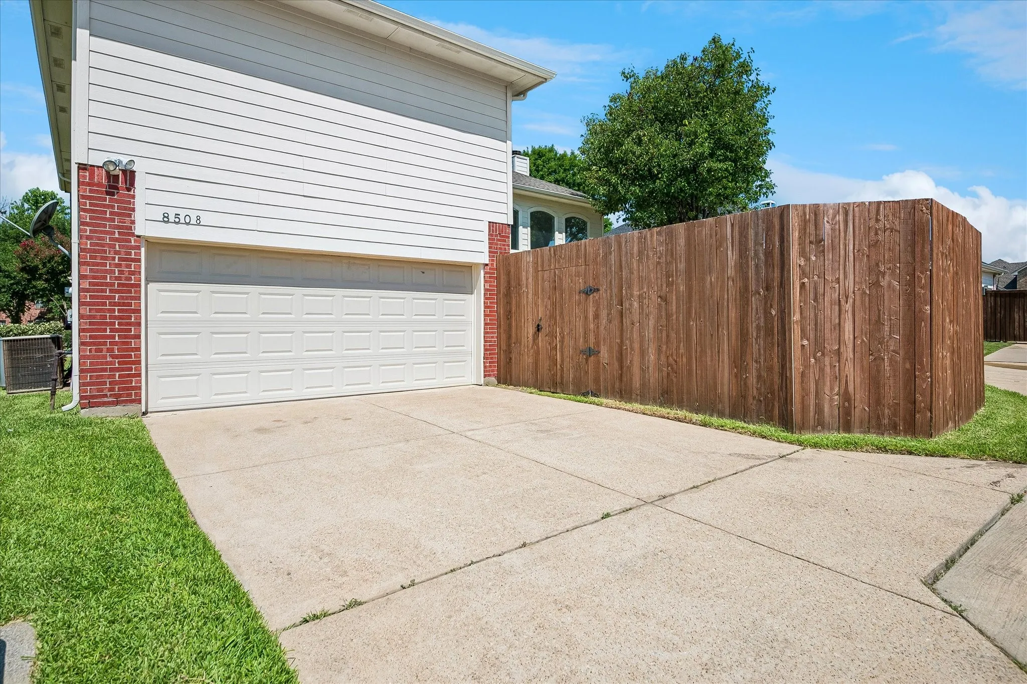 Two-car garage with a paneled door, brick accents, and a concrete driveway showing Alley and corner lot