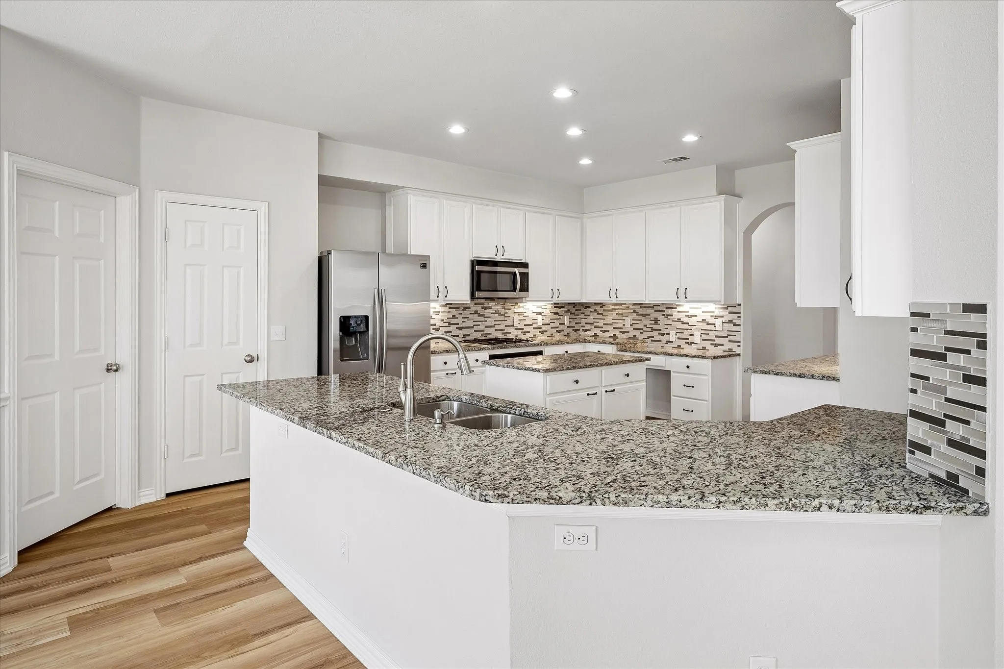 Kitchen featuring a breakfast bar with granite countertops, stainless steel appliances, a mosaic tile backsplash, and white cabinetry