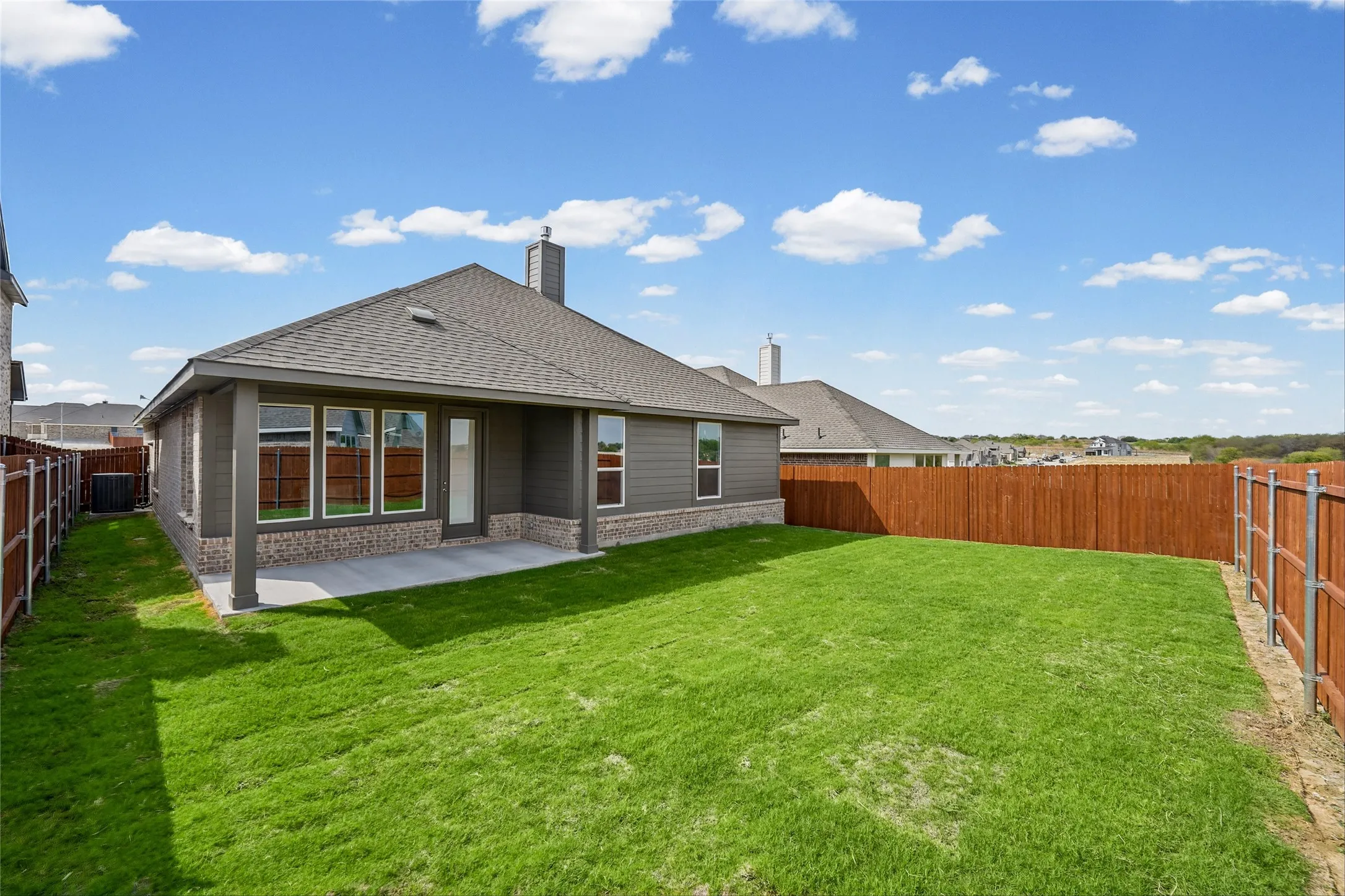 Expansive green lawn with a privacy fence, covered patio, and a shingled roofline