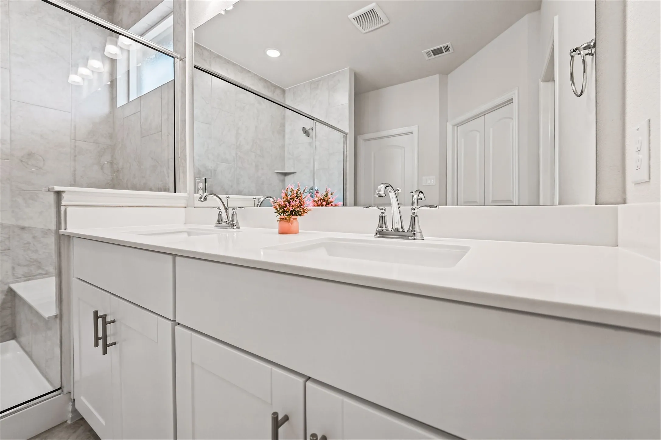 Dual vanity with white cabinetry and chrome hardware, white solid surface countertops, undermount sinks, and a walk-in shower with tile surround and glass enclosure