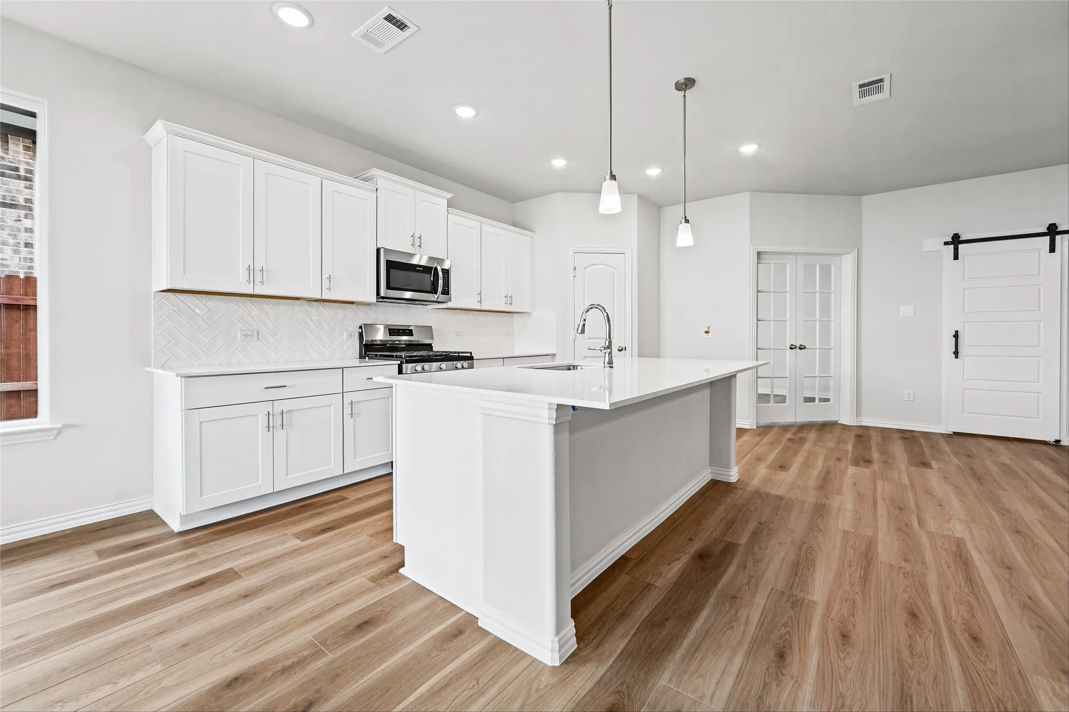 Modern kitchen featuring white cabinetry, stainless steel appliances, a center island with pendant lighting, wood-finish flooring, and a sliding barn door