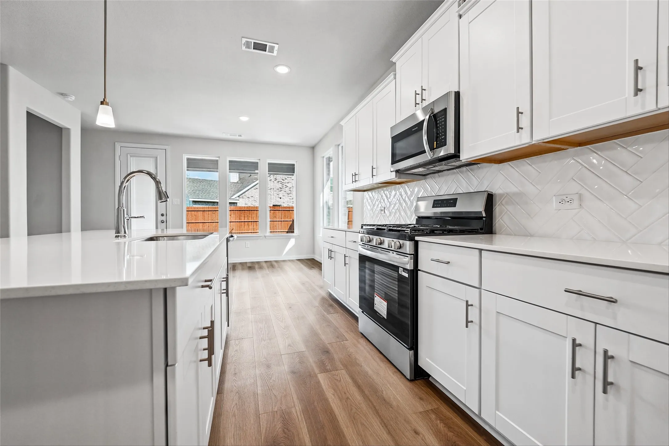 Kitchen featuring white cabinetry, wood-finish flooring, stainless steel appliances, and a herringbone tile backsplash