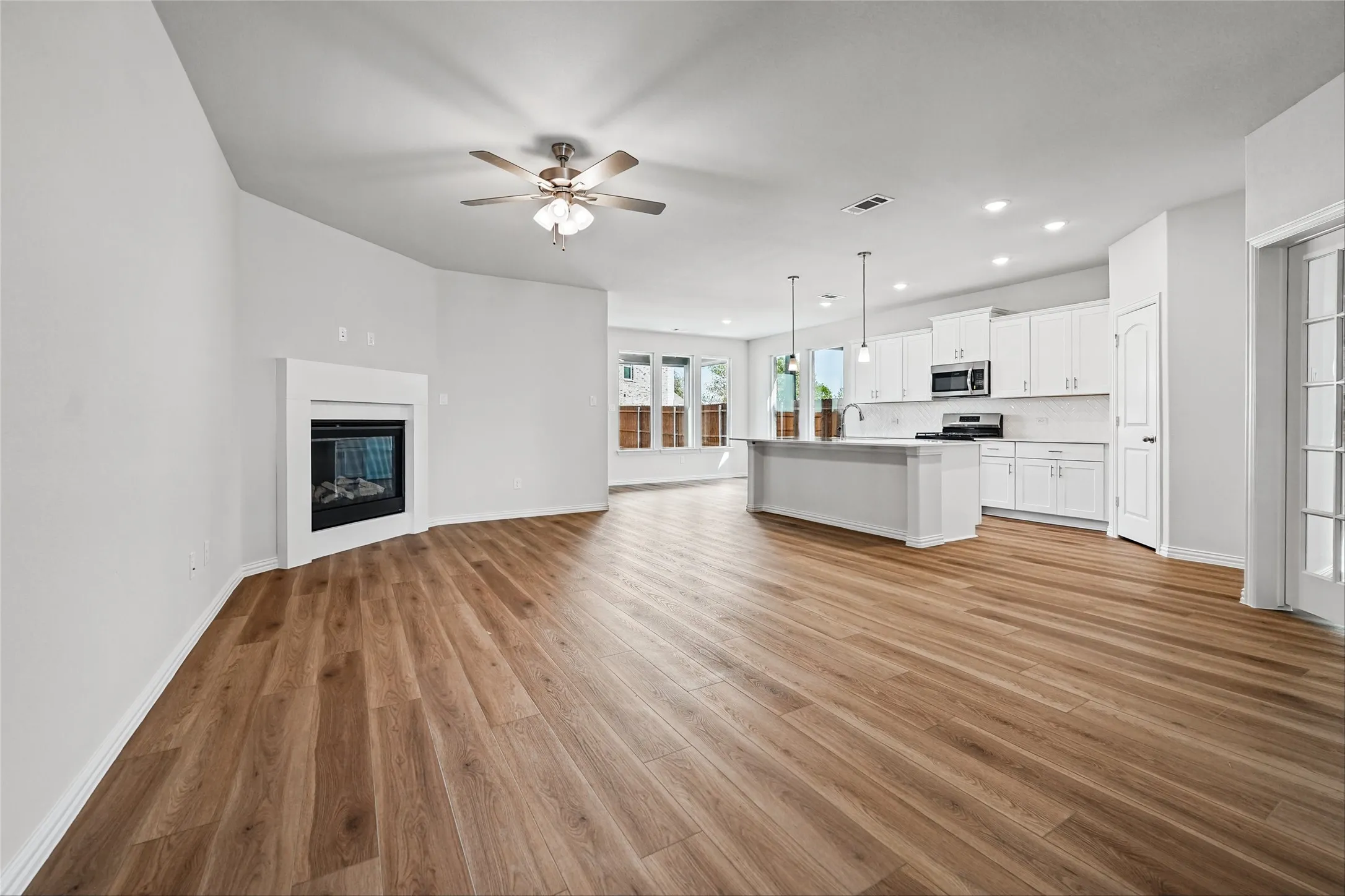 Open-concept living space featuring wood-finish flooring, a corner fireplace, and a ceiling fan