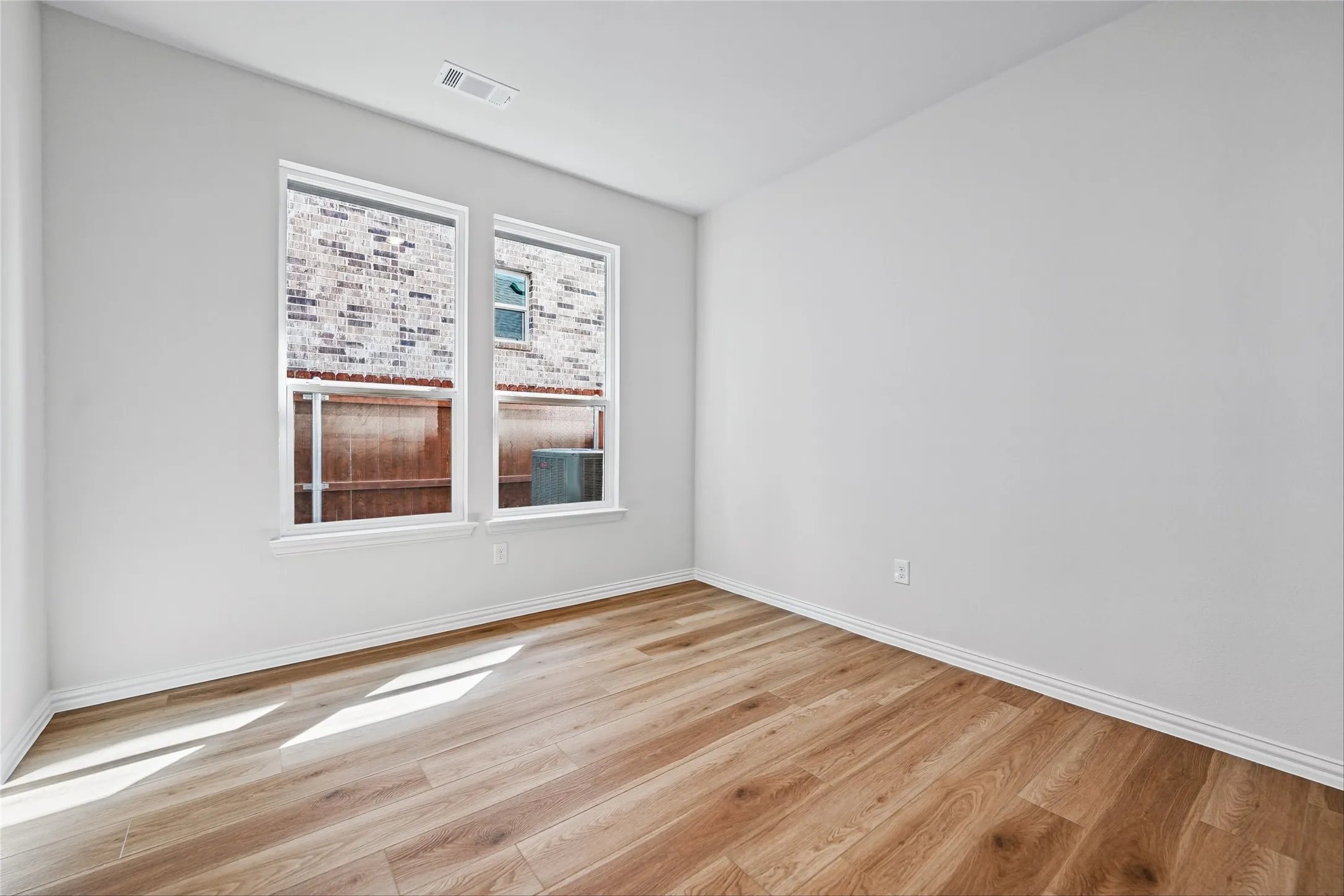 Light wood-finish flooring, white painted walls, and two windows with white trim