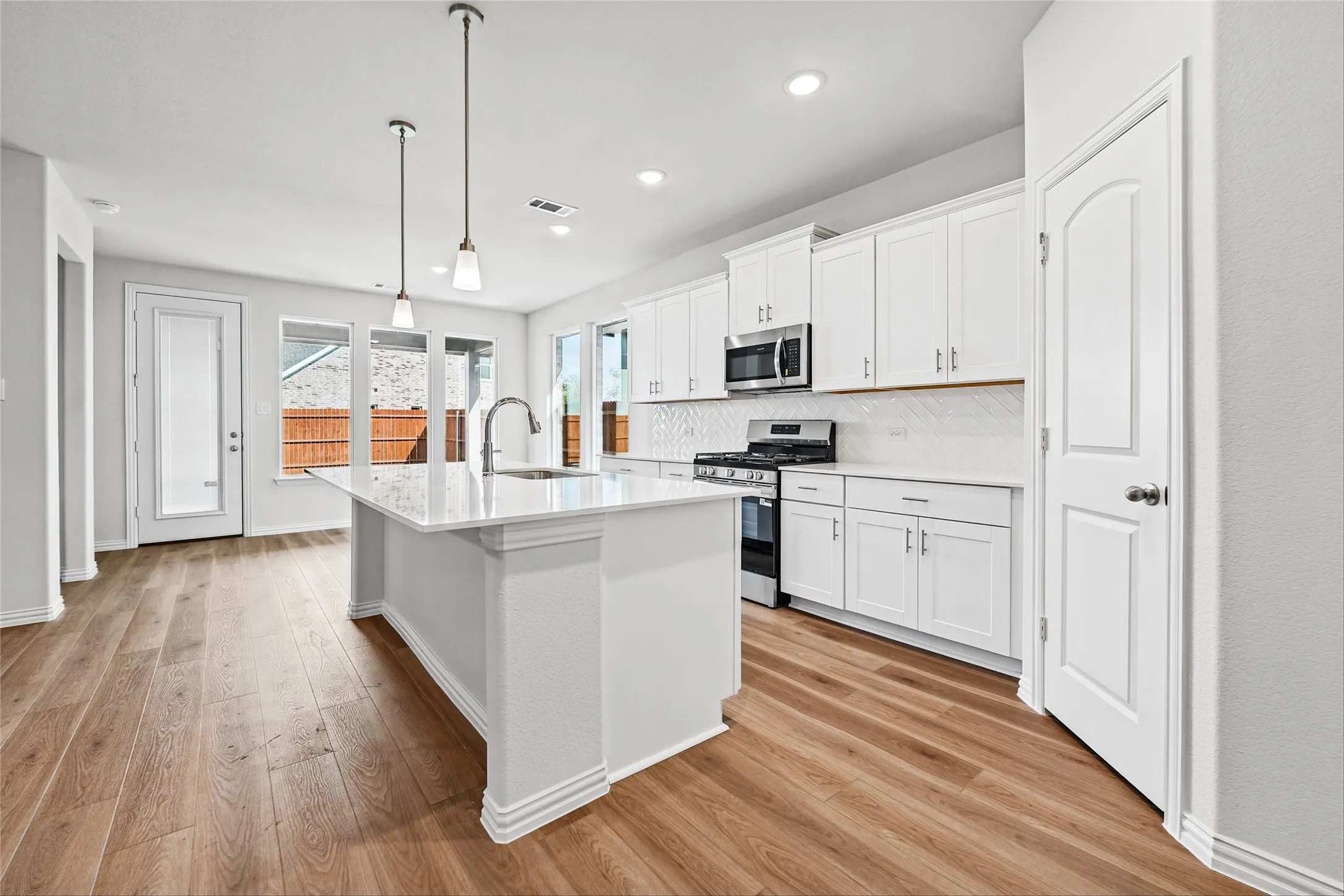 Kitchen featuring white cabinetry, a central island with an integrated sink, stainless steel appliances, and wood-finish flooring