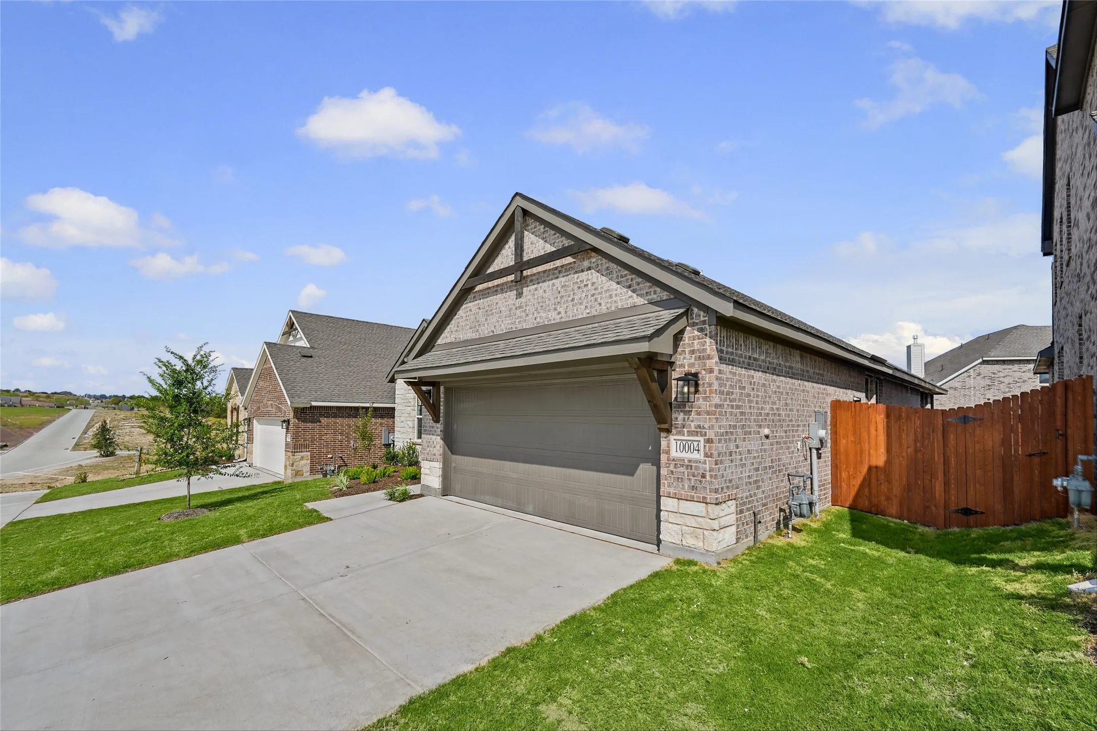 Brick and stone exterior with a gabled roofline, attached garage, concrete driveway, and a wood privacy fence