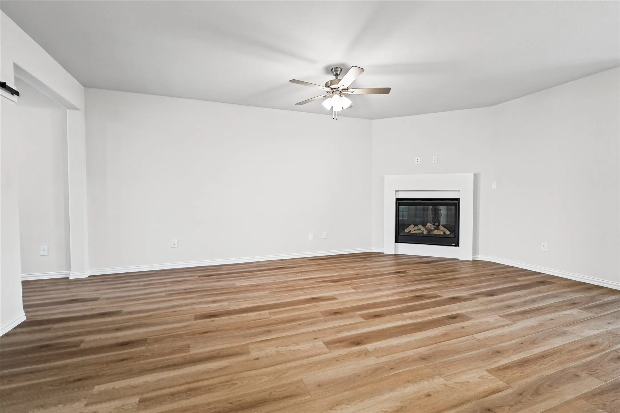 Wood-finish flooring, built-in fireplace, ceiling fan with integrated lighting, and crisp white walls