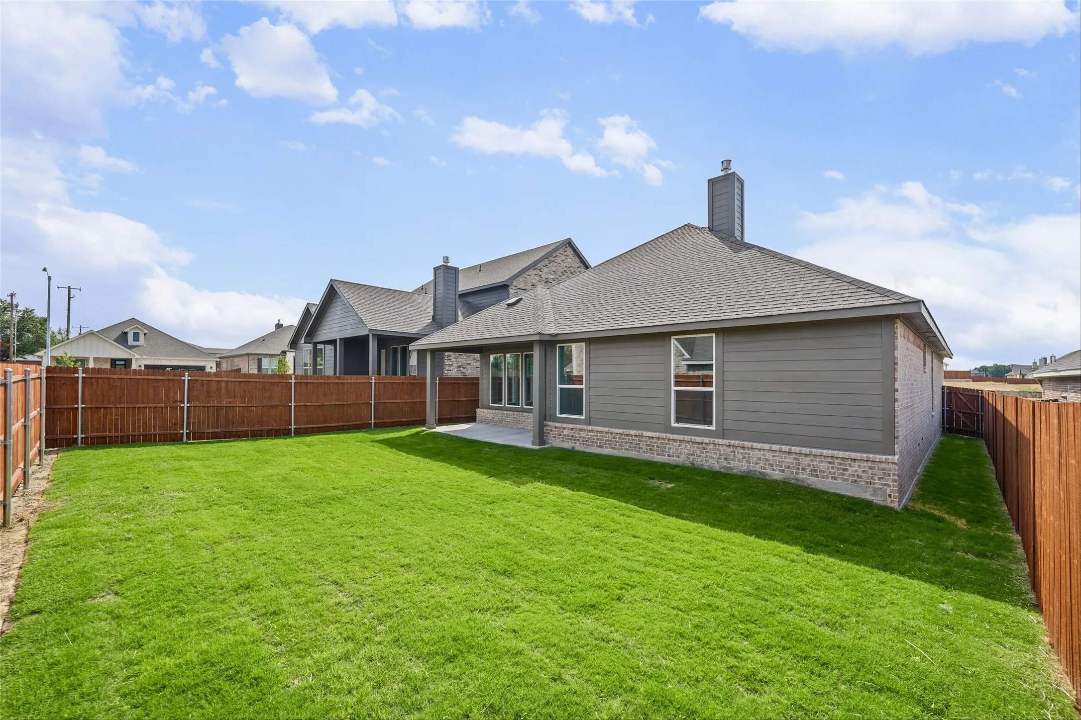 Expansive backyard featuring a manicured lawn, wood privacy fencing, a covered concrete patio, and a shingled roofline