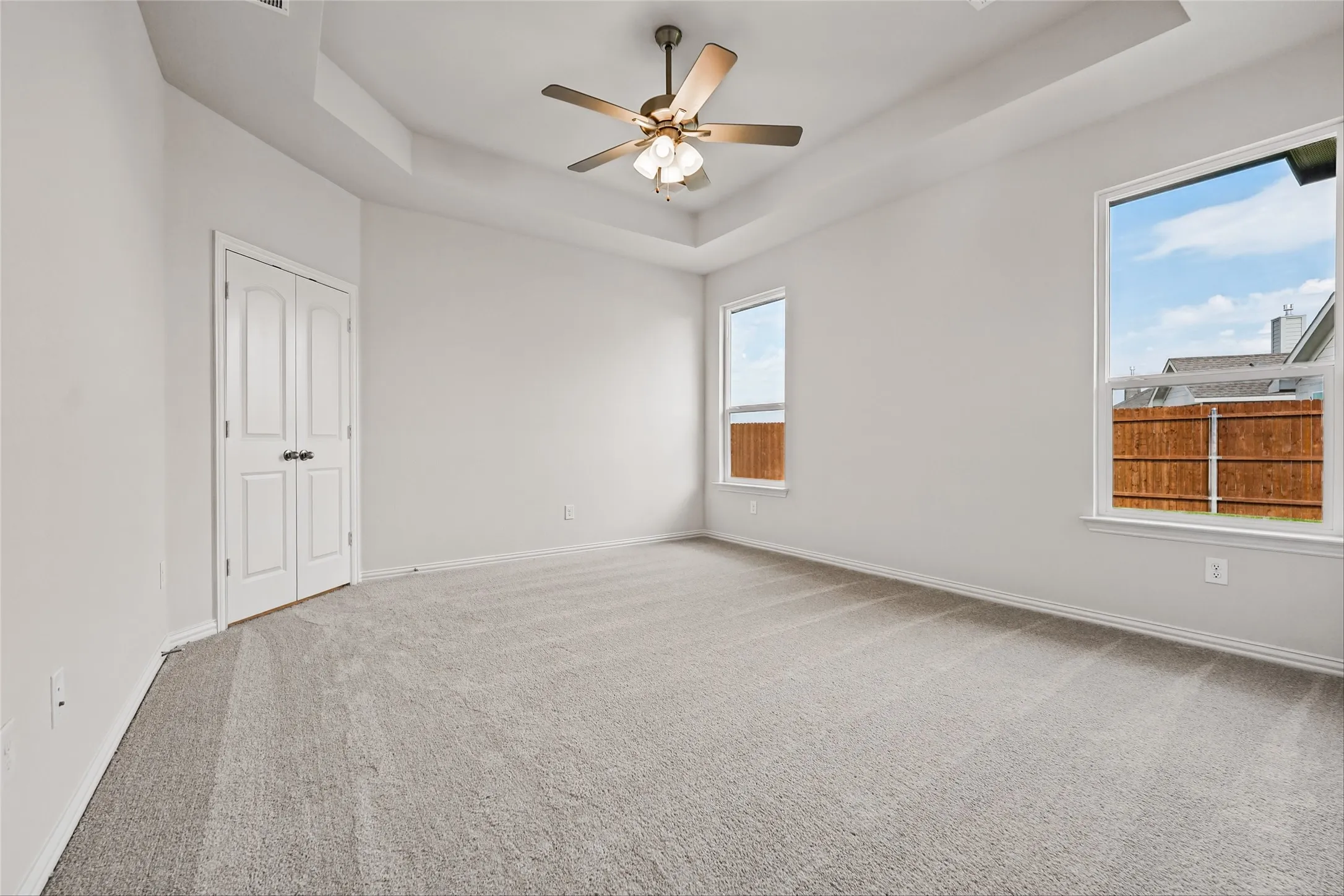 Recessed tray ceiling with a ceiling fan, light gray carpet flooring, and two windows