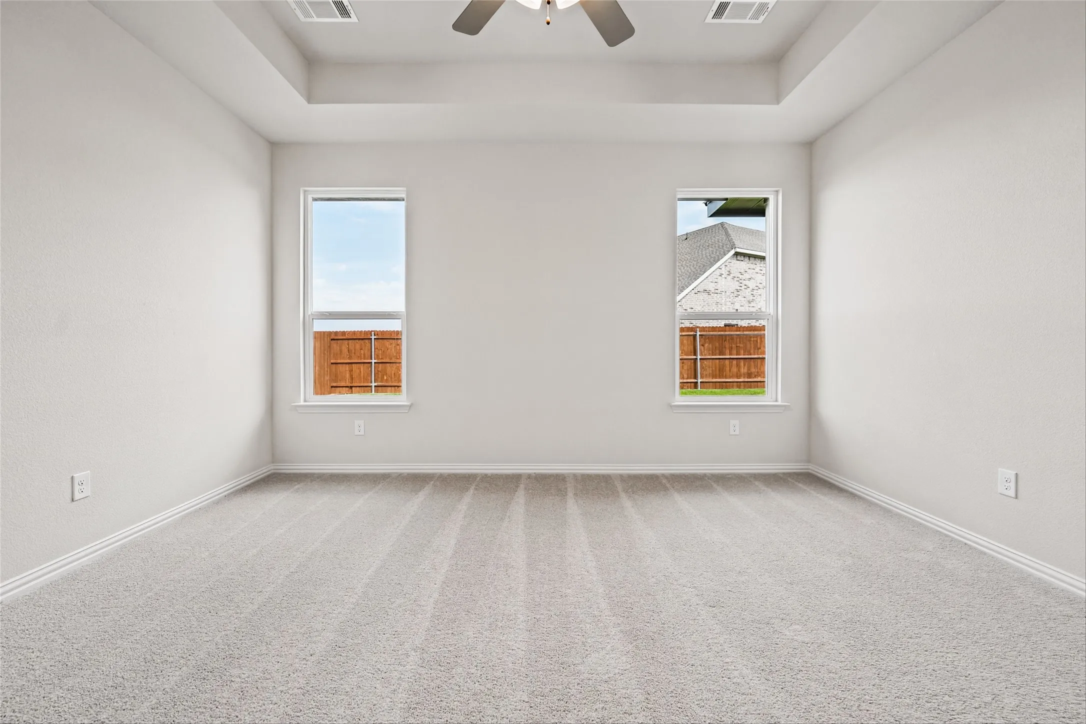 Tray ceiling with a ceiling fan, two windows, and light gray carpeting