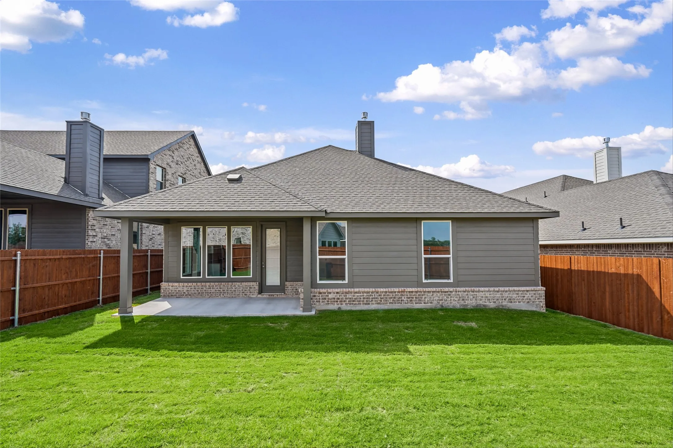 Expansive green lawn with a covered concrete patio, grey siding, and a brick foundation