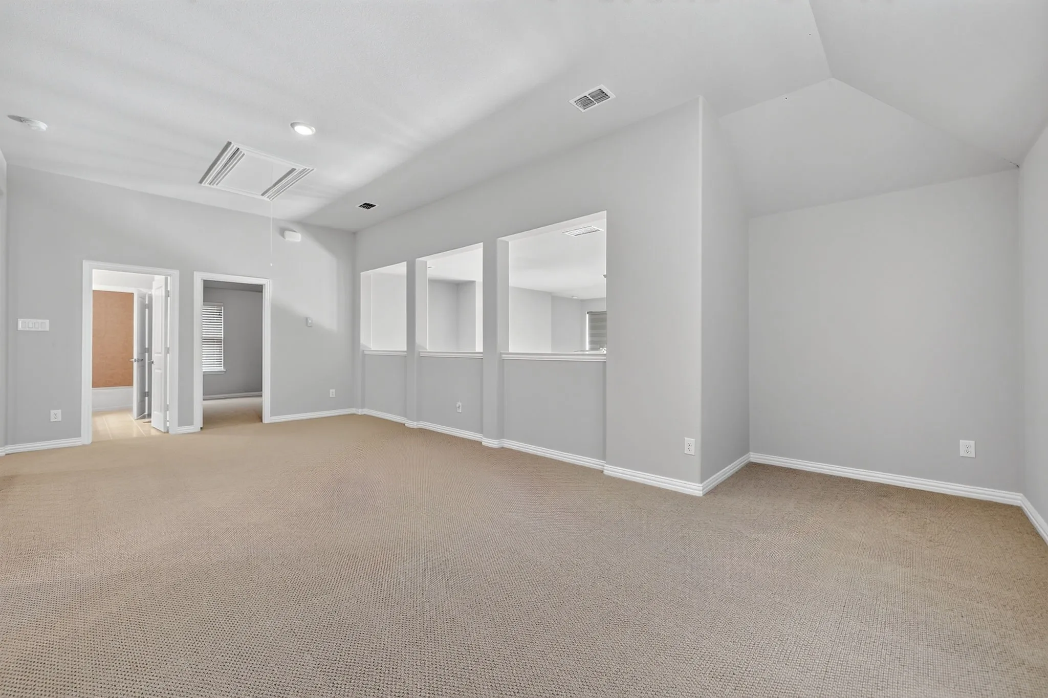 Spacious carpeted room featuring light gray walls, white baseboards, and a vaulted ceiling