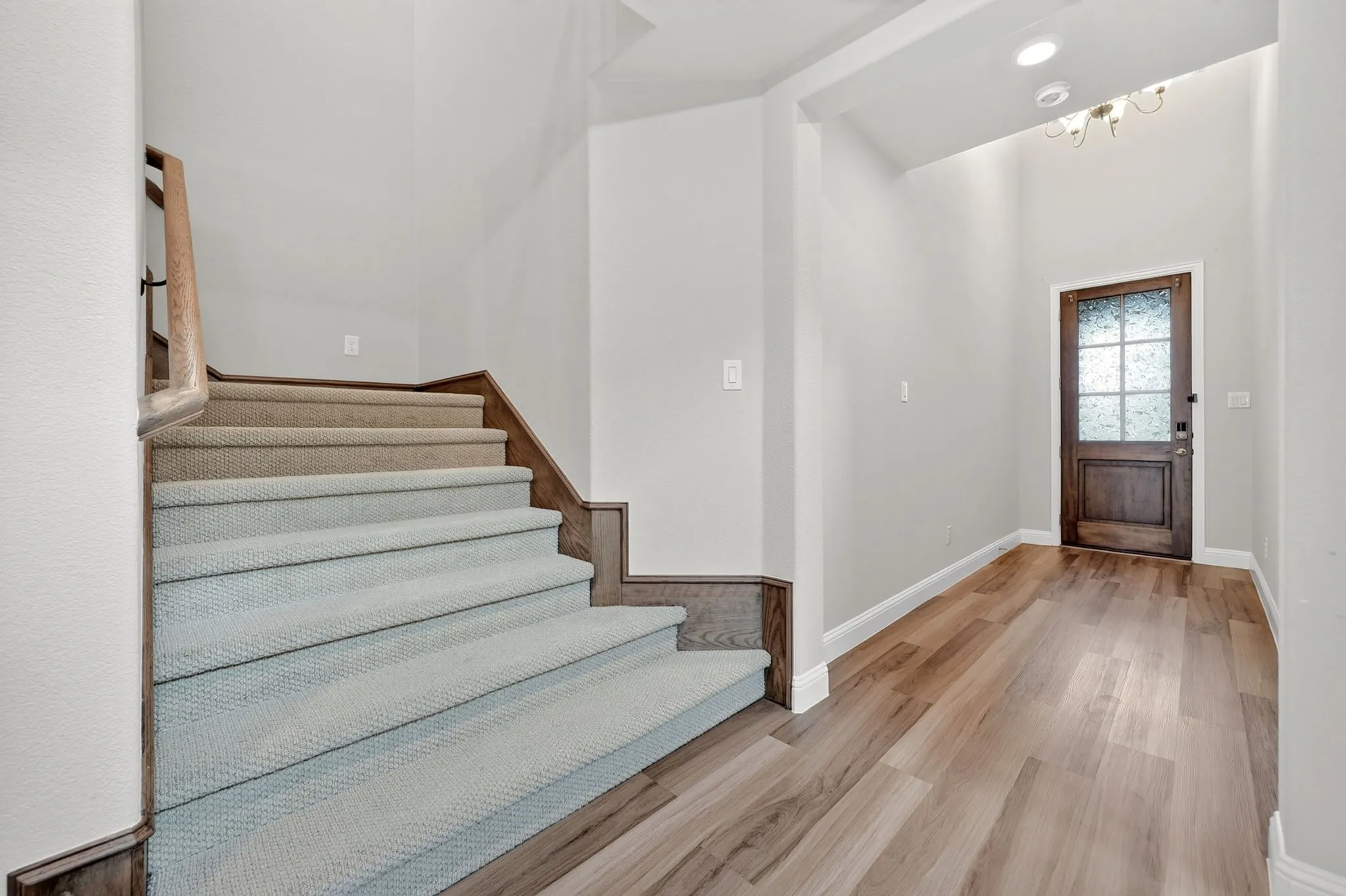 Entryway featuring wood-finish flooring, a solid wood entry door with frosted glass panes, and a carpeted staircase with wood risers and a wood handrail