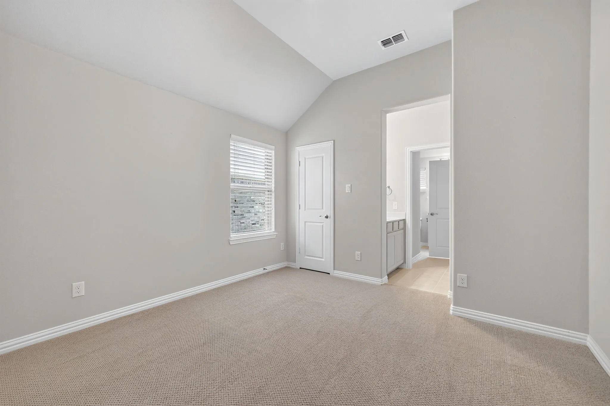 Carpeted room featuring a vaulted ceiling, a single window with blinds, and white trim throughout