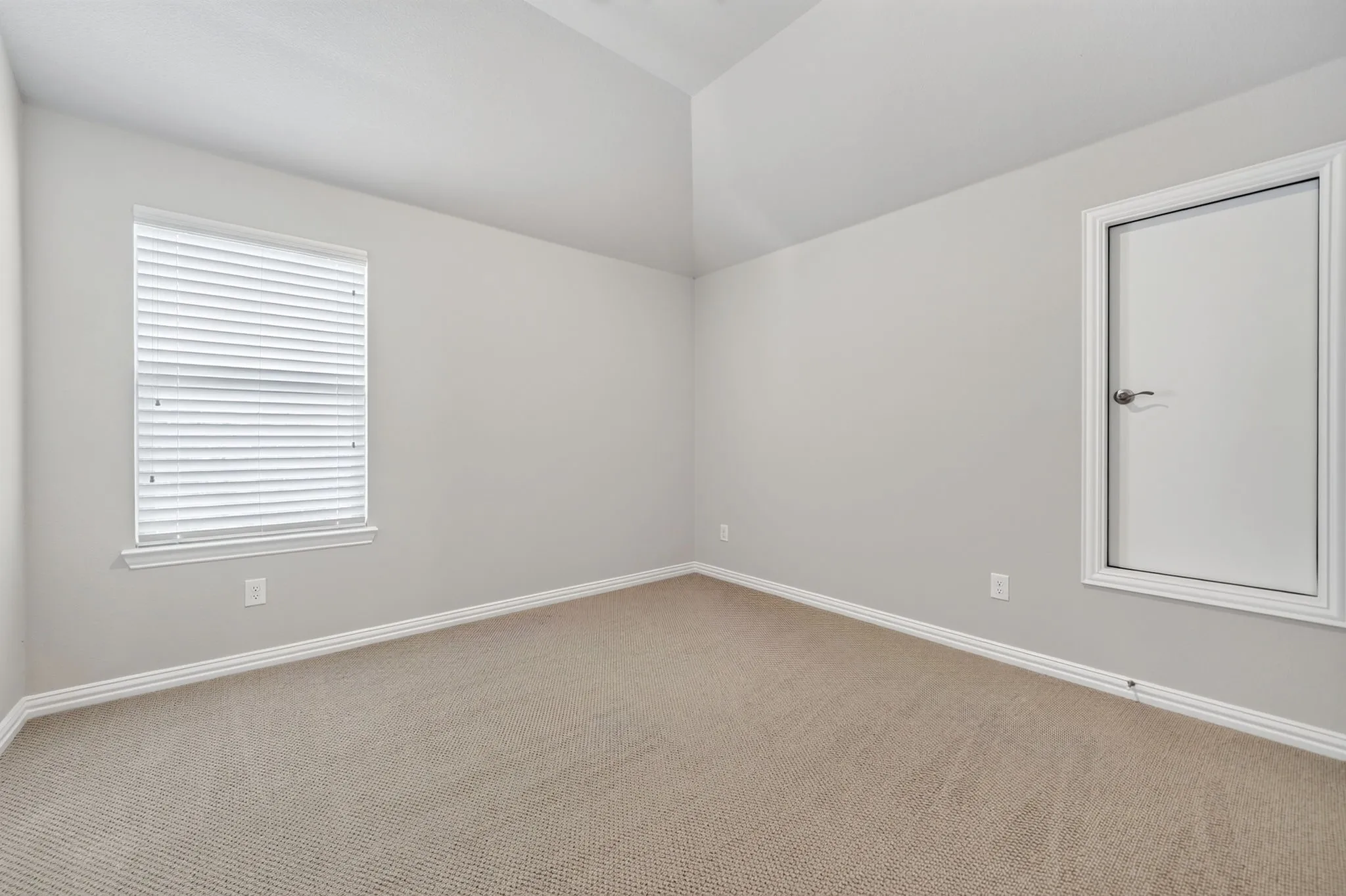 Room featuring vaulted ceilings, neutral-toned carpet, a window with blinds, and a white door with trim