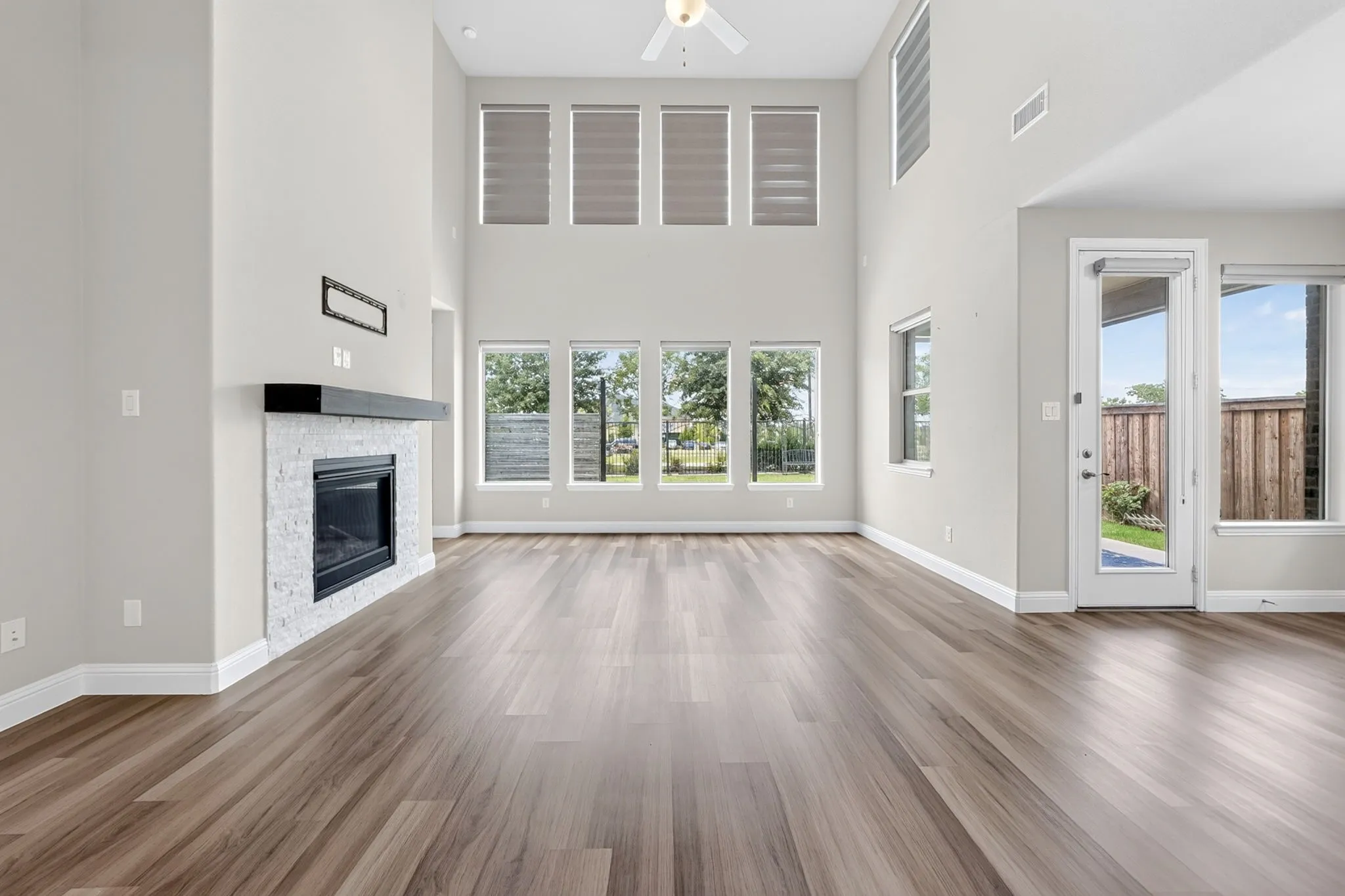 Spacious living area featuring wood-finish flooring, a white stacked stone fireplace with a dark wood mantel, and a dual-height ceiling