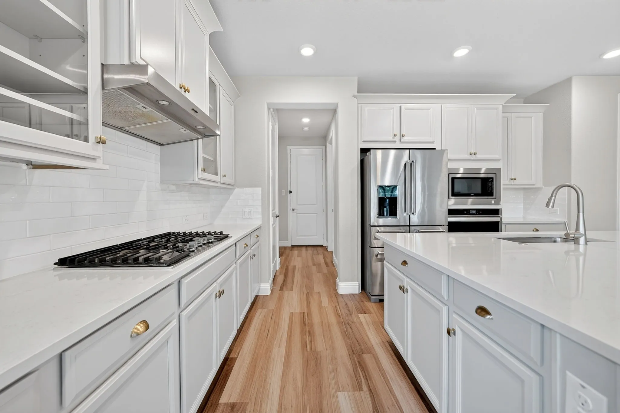 Gourmet kitchen featuring a gas range cooktop, stainless steel appliances, light-toned cabinetry, a spacious island with an integrated sink, and wood-finish flooring