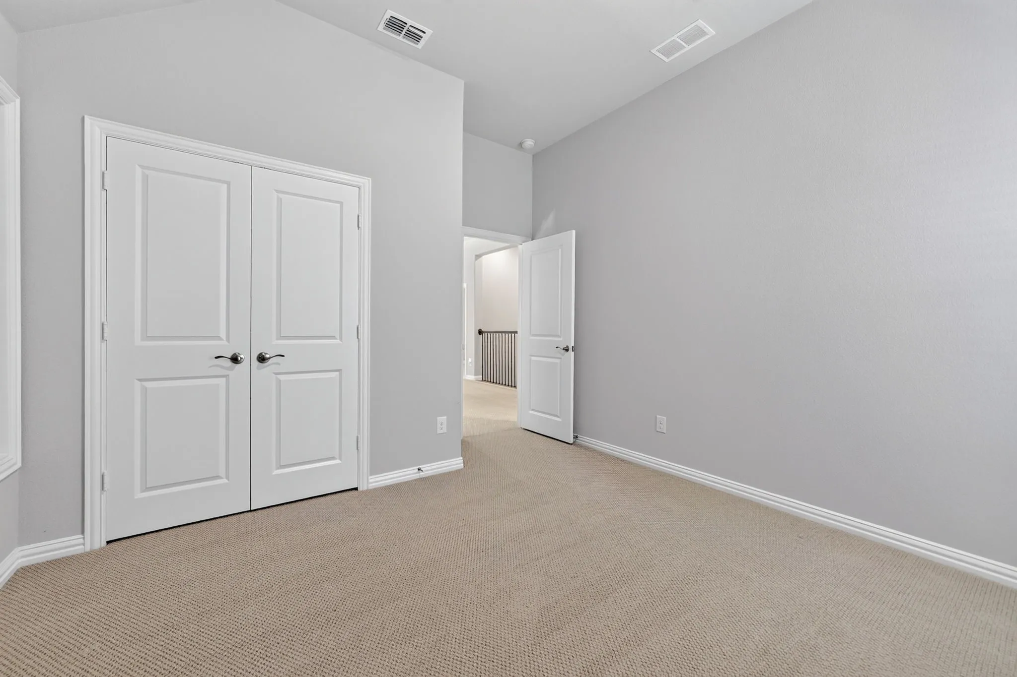 Neutral-toned carpet flooring in a room featuring a vaulted ceiling and a double-door closet with black hardware