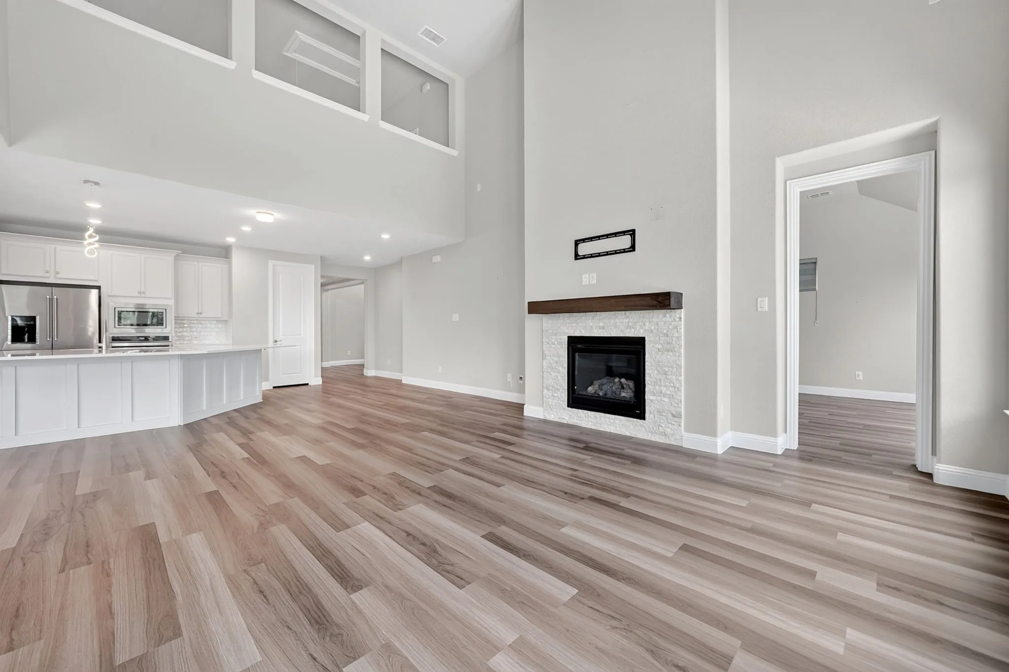 Open-concept living space featuring wood-finish flooring, a contemporary fireplace with a stone surround and wood mantel, and a kitchen island with a white countertop and white cabinetry