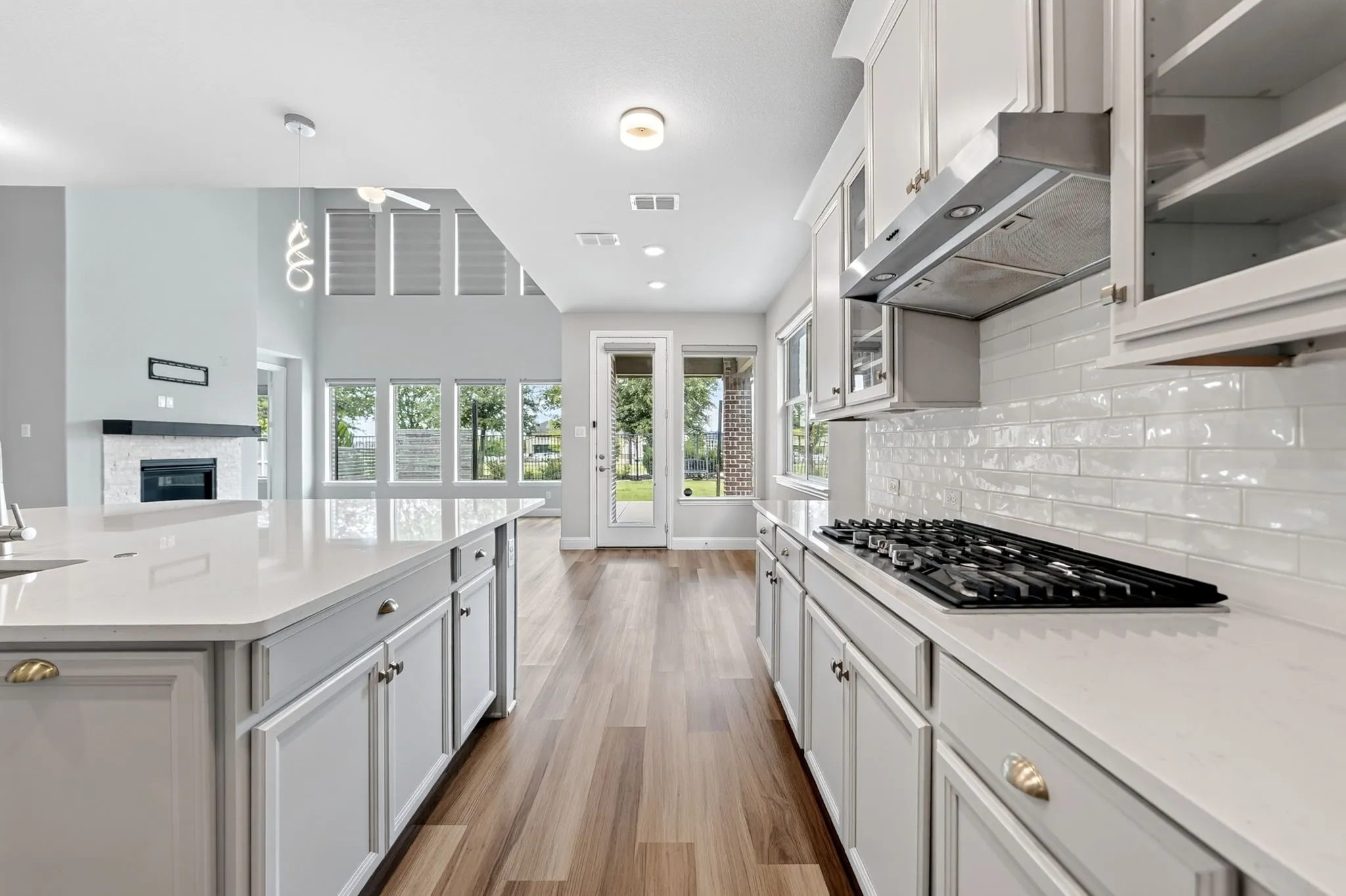 Open-concept kitchen featuring light-toned cabinetry, a gas cooktop with an overhead range hood, white subway tile backsplash, and light-colored countertops