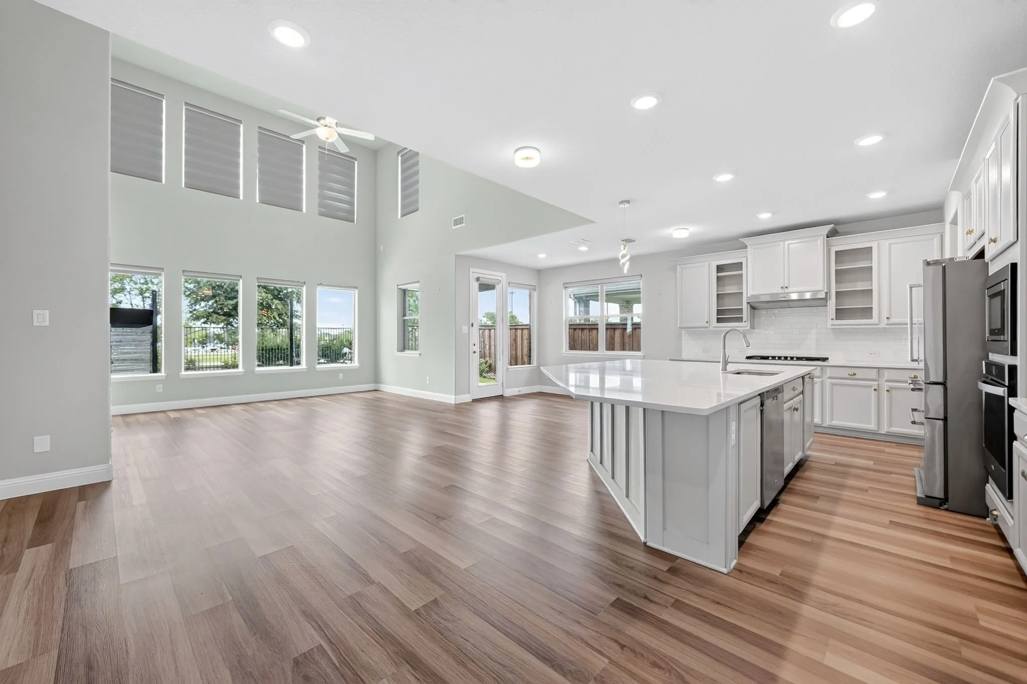 Open-concept living area featuring high ceilings, wood-finish flooring, and abundant natural light from numerous windows