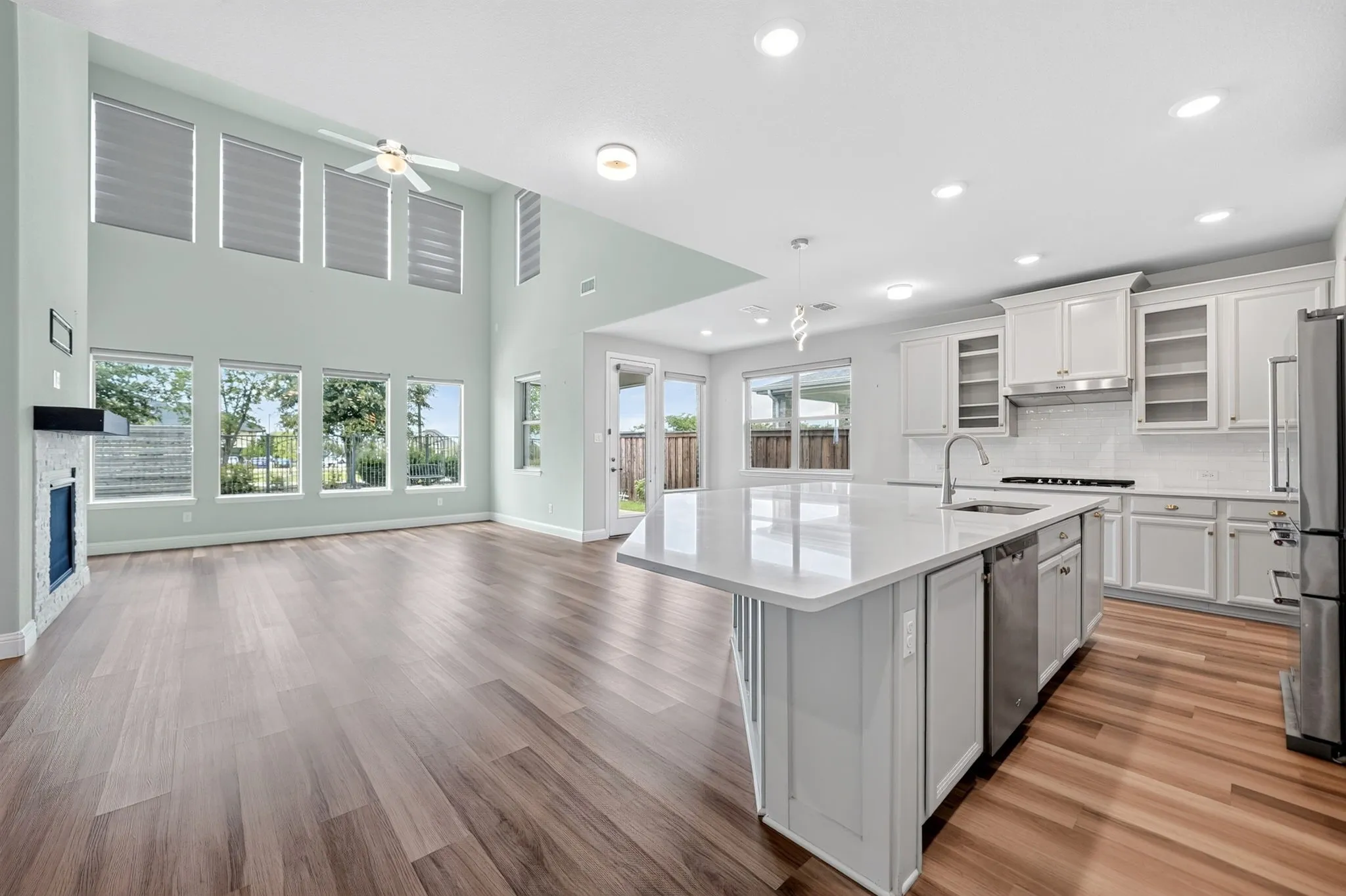 Open-concept living area featuring high ceilings, wood-finish flooring, and a fireplace with a stone surround