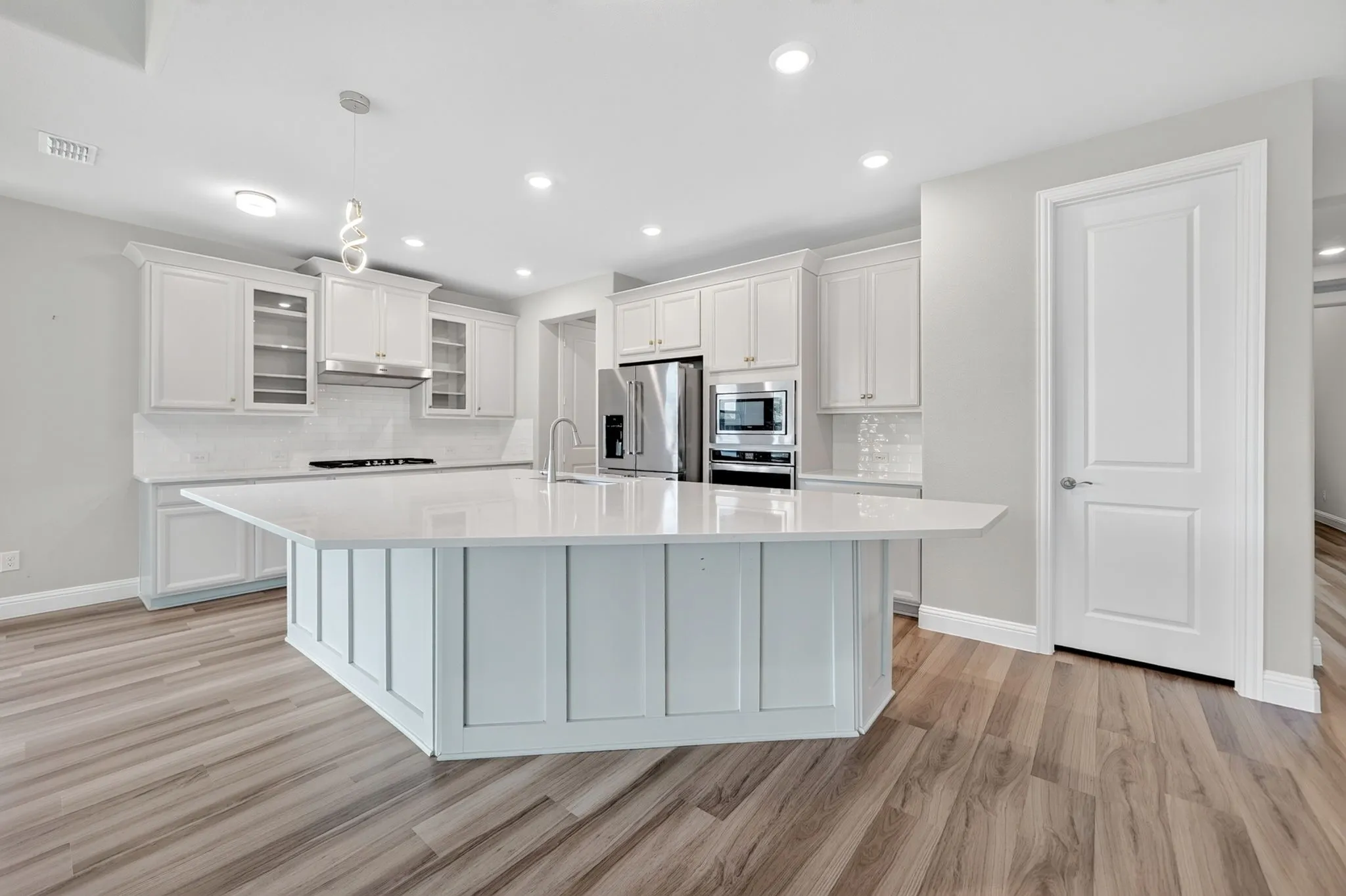 Spacious kitchen featuring a large central island with light-toned countertop, wood-finish flooring, white cabinetry, and stainless steel appliances