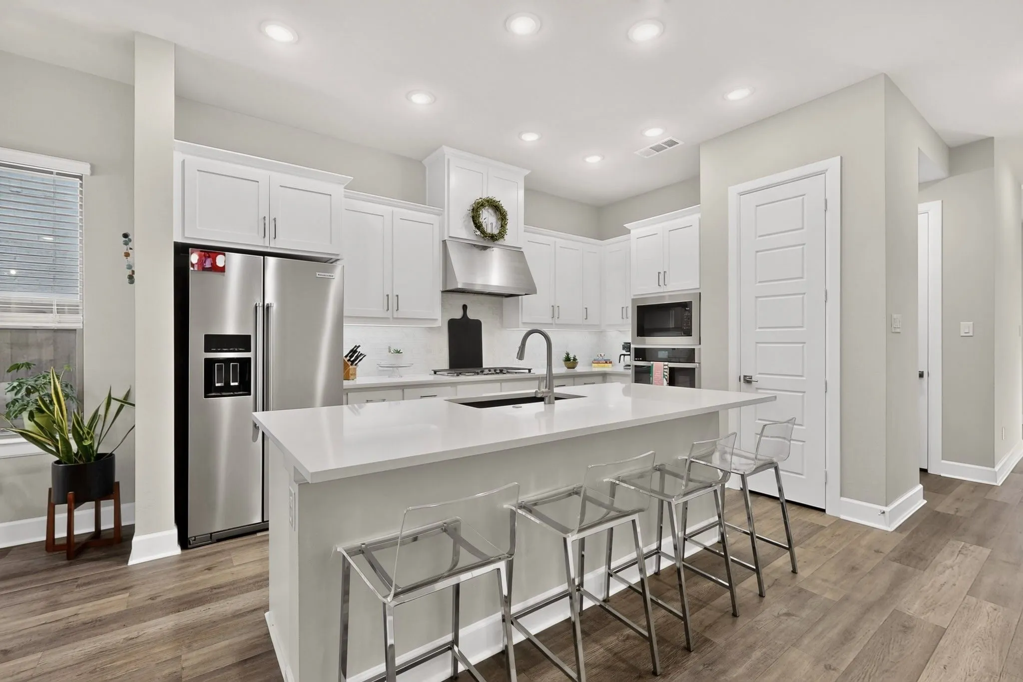 Modern kitchen featuring an expansive island with countertop seating, stainless steel appliances, abundant white cabinetry, recessed lighting, and wood-finish flooring