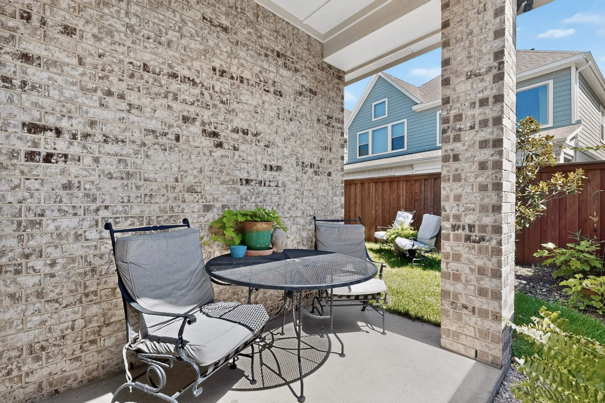 Covered concrete patio featuring a brick exterior wall and columns