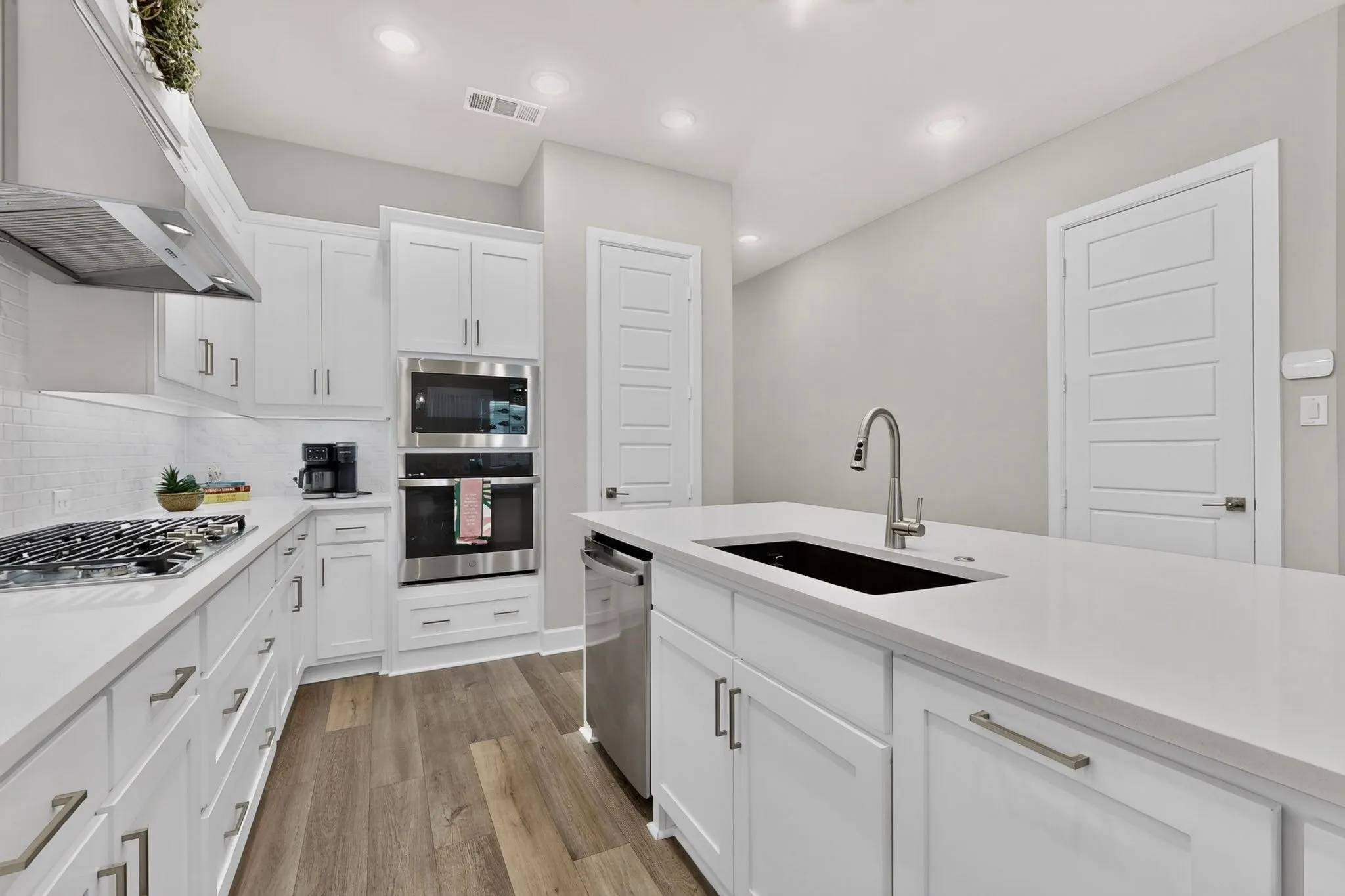 Contemporary kitchen featuring white cabinetry, light-toned countertops, and wood-finish flooring
