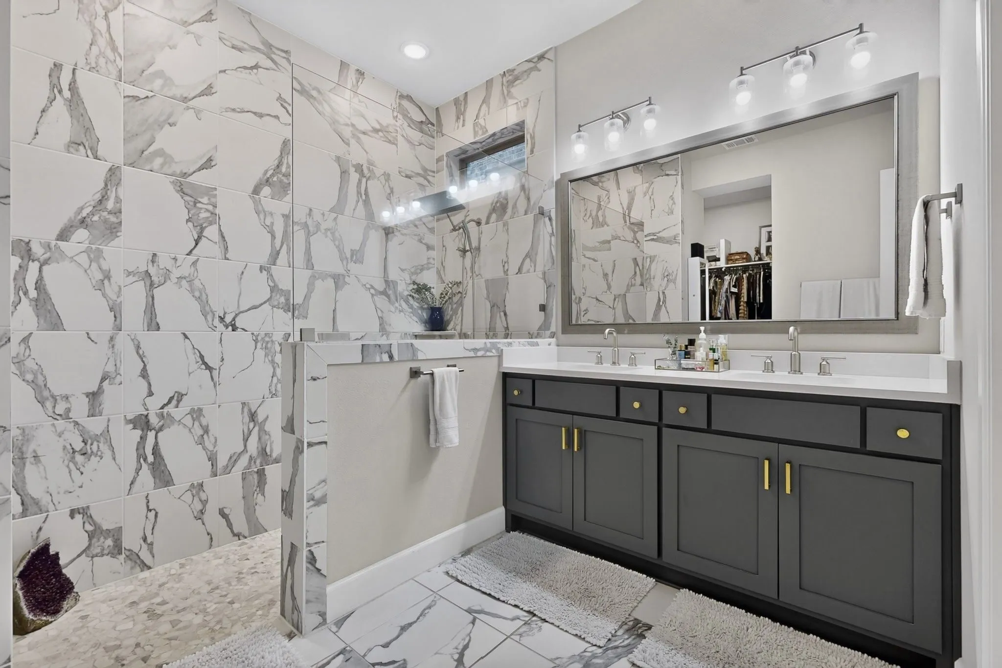Spacious bathroom featuring a dual vanity with a white countertop and grey cabinetry, a large framed mirror, and two contemporary light fixtures