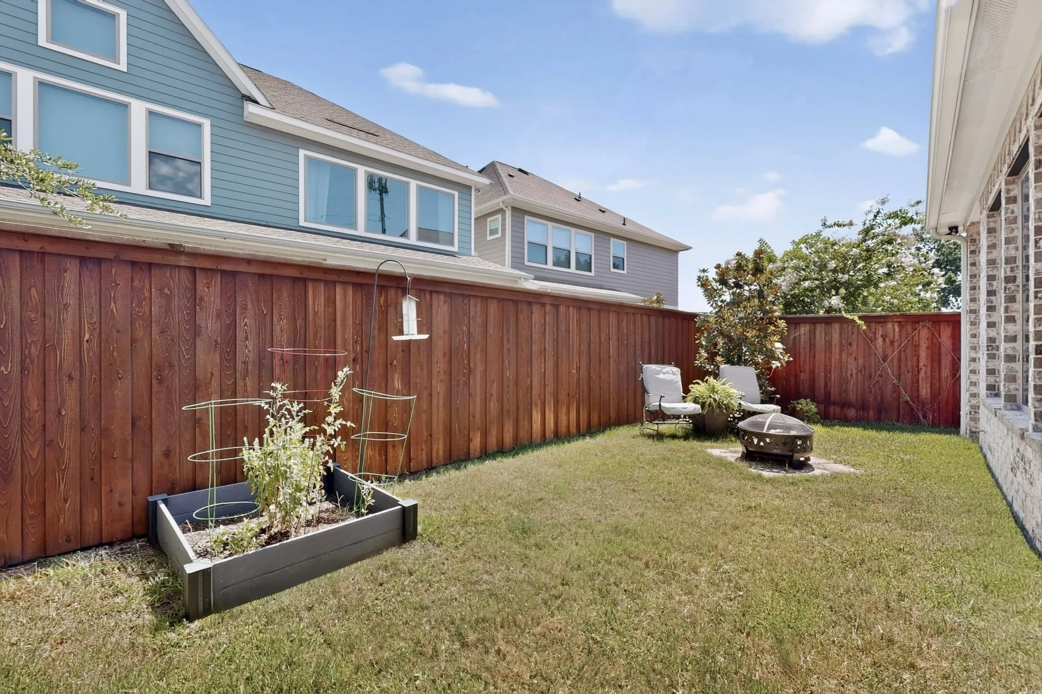Fenced backyard with established lawn, a raised garden bed, and a fire pit area