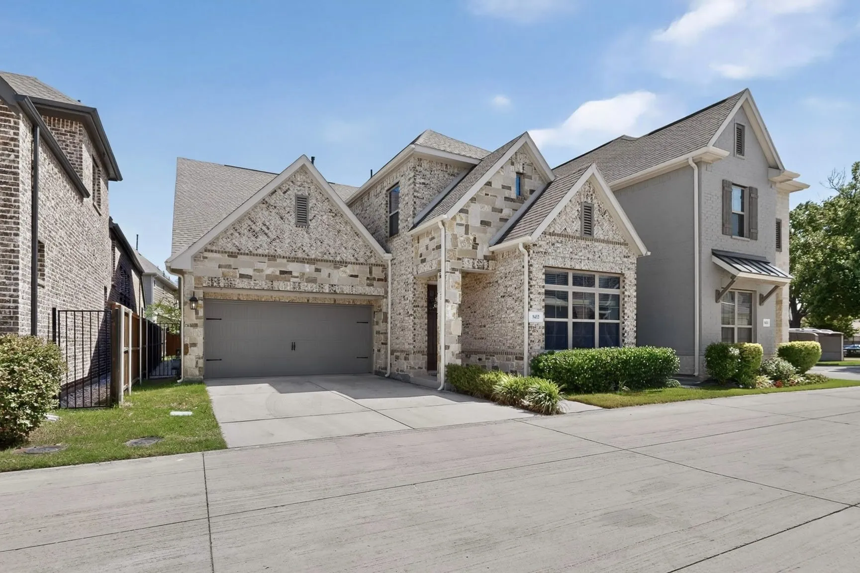Stone and brick facade residence featuring a two-car garage, pitched roofline, and front landscaping