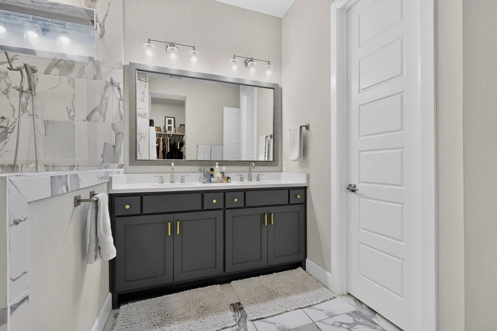 Bathroom featuring a dual vanity with a white countertop and dark cabinetry, large framed mirror, and marble-look tile flooring