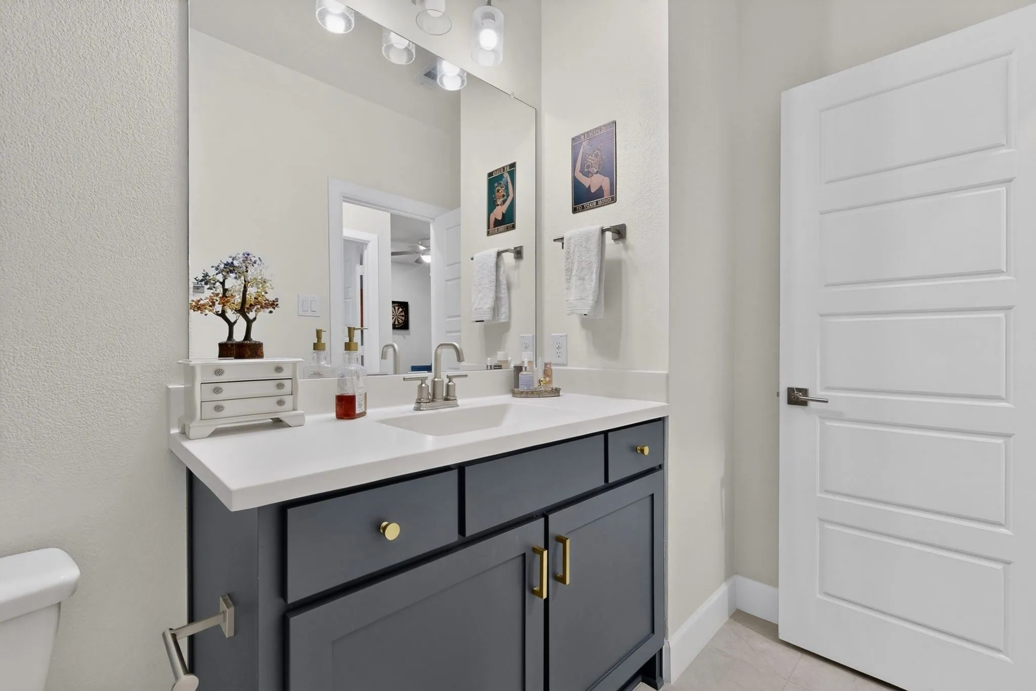 Modern bathroom vanity featuring a rectangular undermount sink, a light-toned countertop, a dark gray cabinet with golden hardware, and a contemporary light fixture