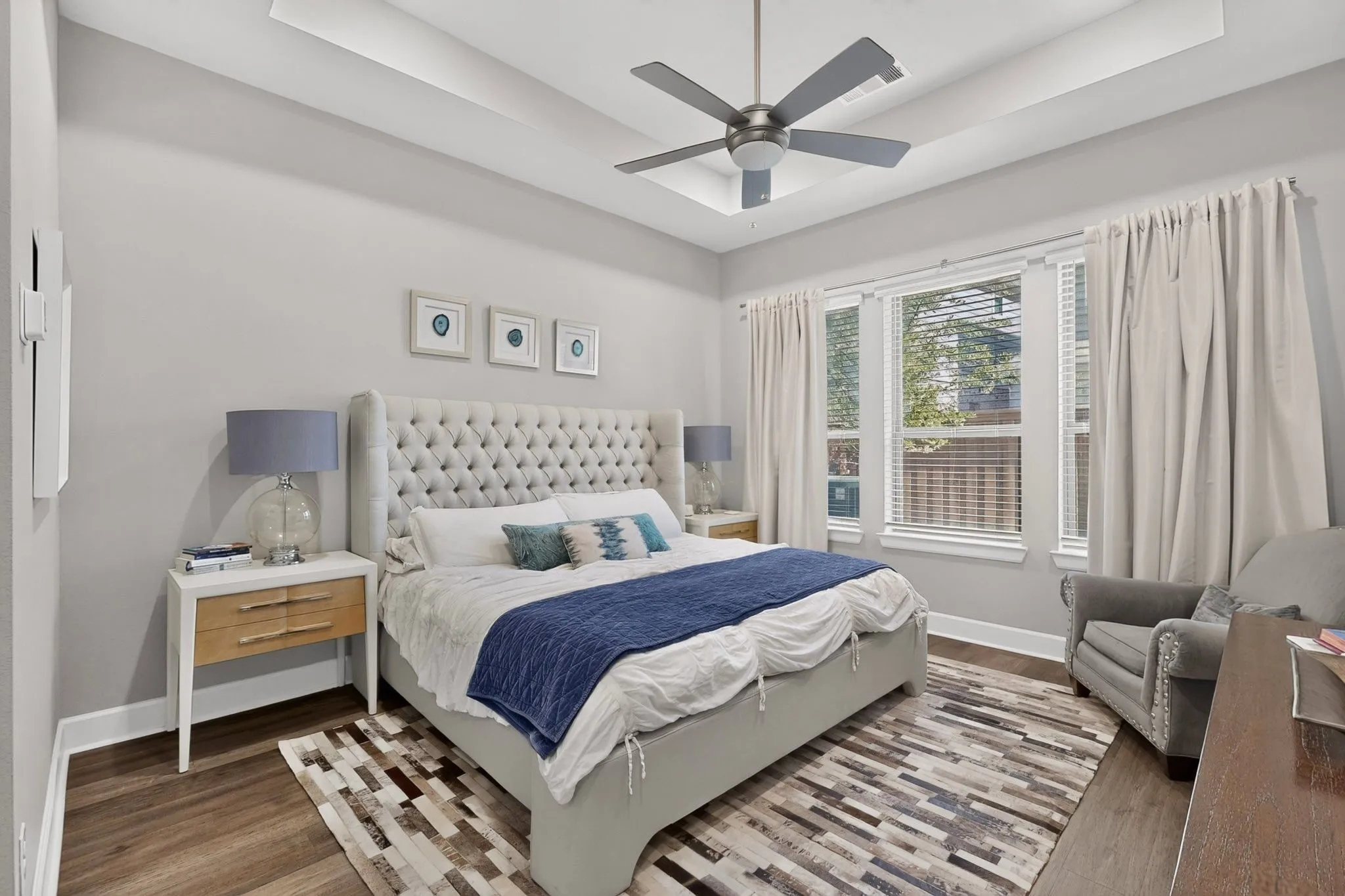 Spacious room featuring wood-finish flooring, a tray ceiling with a ceiling fan, and multiple windows with blinds and drapes