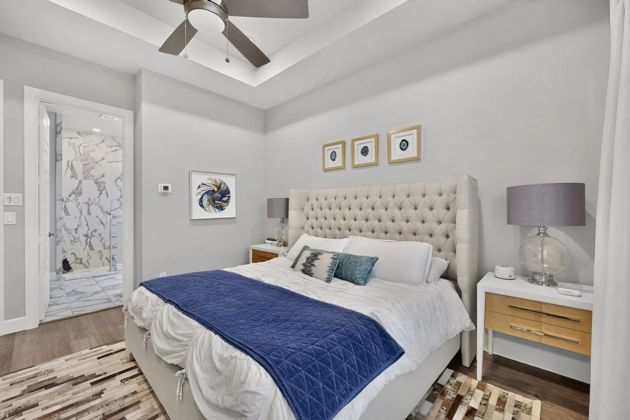 Bedroom featuring a tray ceiling with a ceiling fan, wood-finish flooring, and light gray wall paint