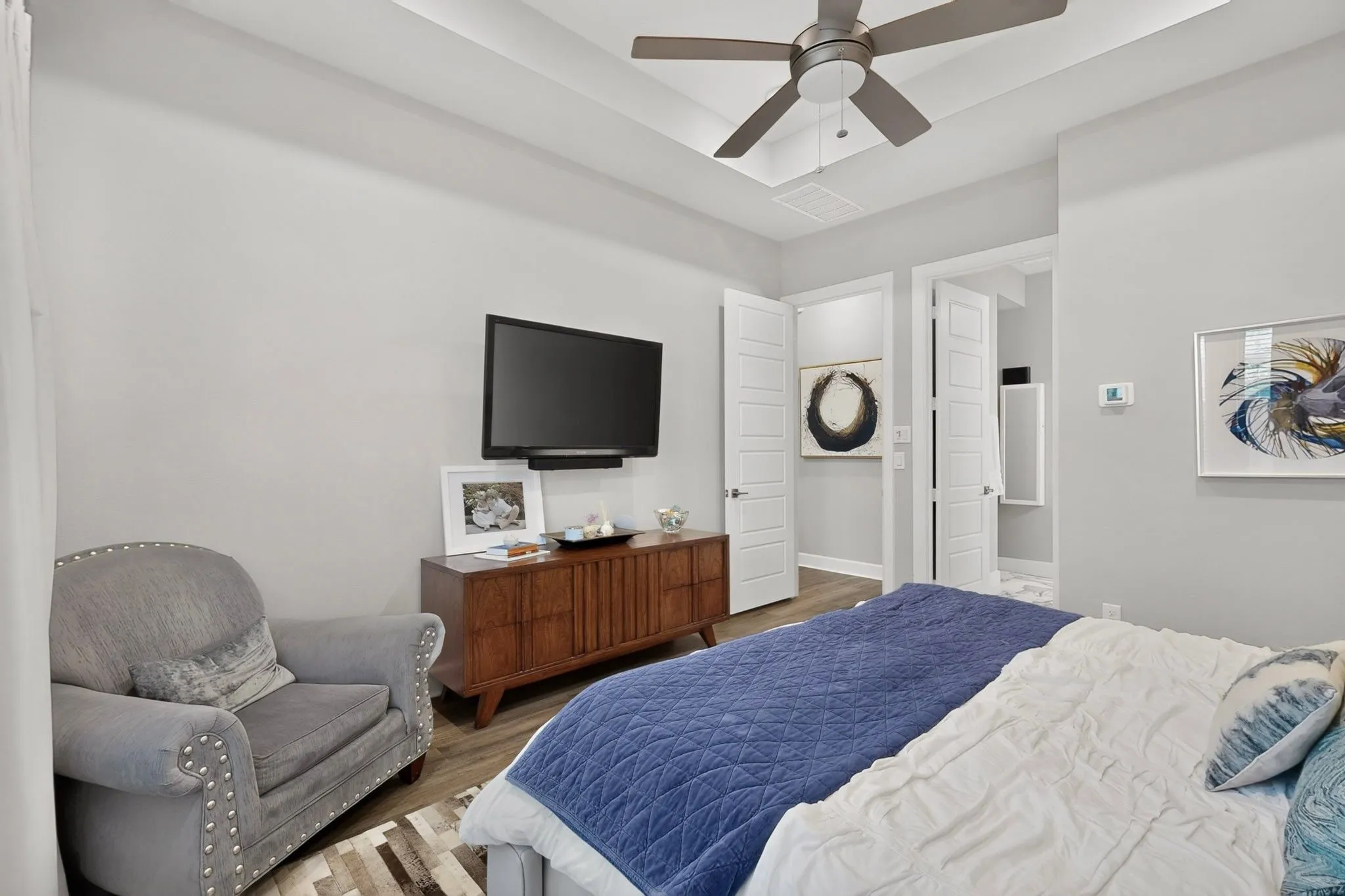 Tray ceiling with a ceiling fan, light gray wall paint, and wood-finish flooring