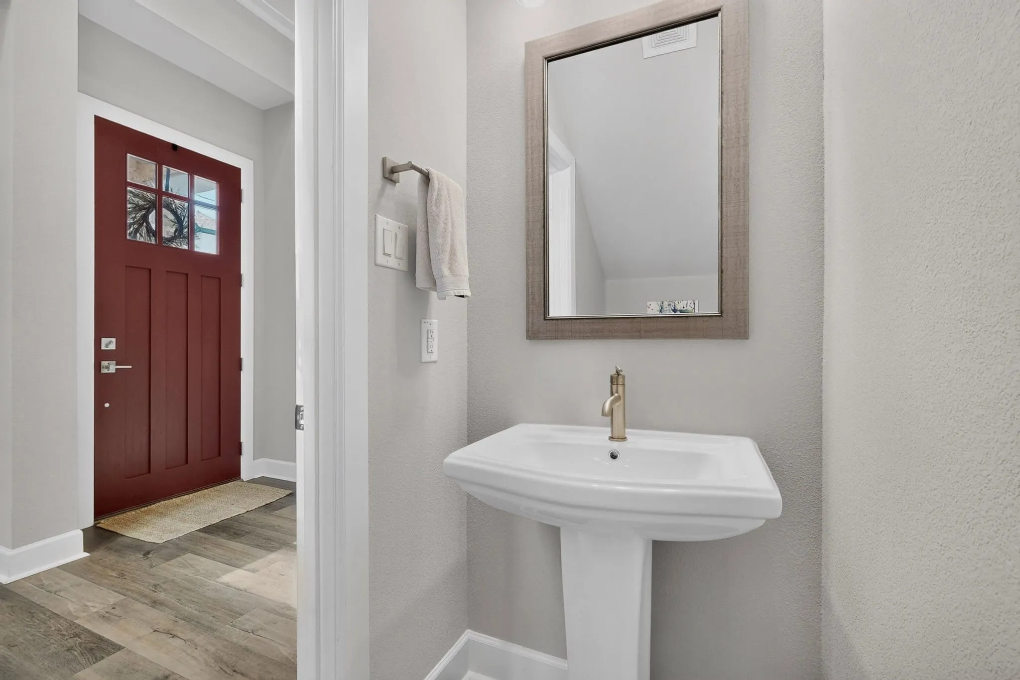 Pedestal sink with gold-tone faucet and a rectangular mirror framed in a light wood-finish