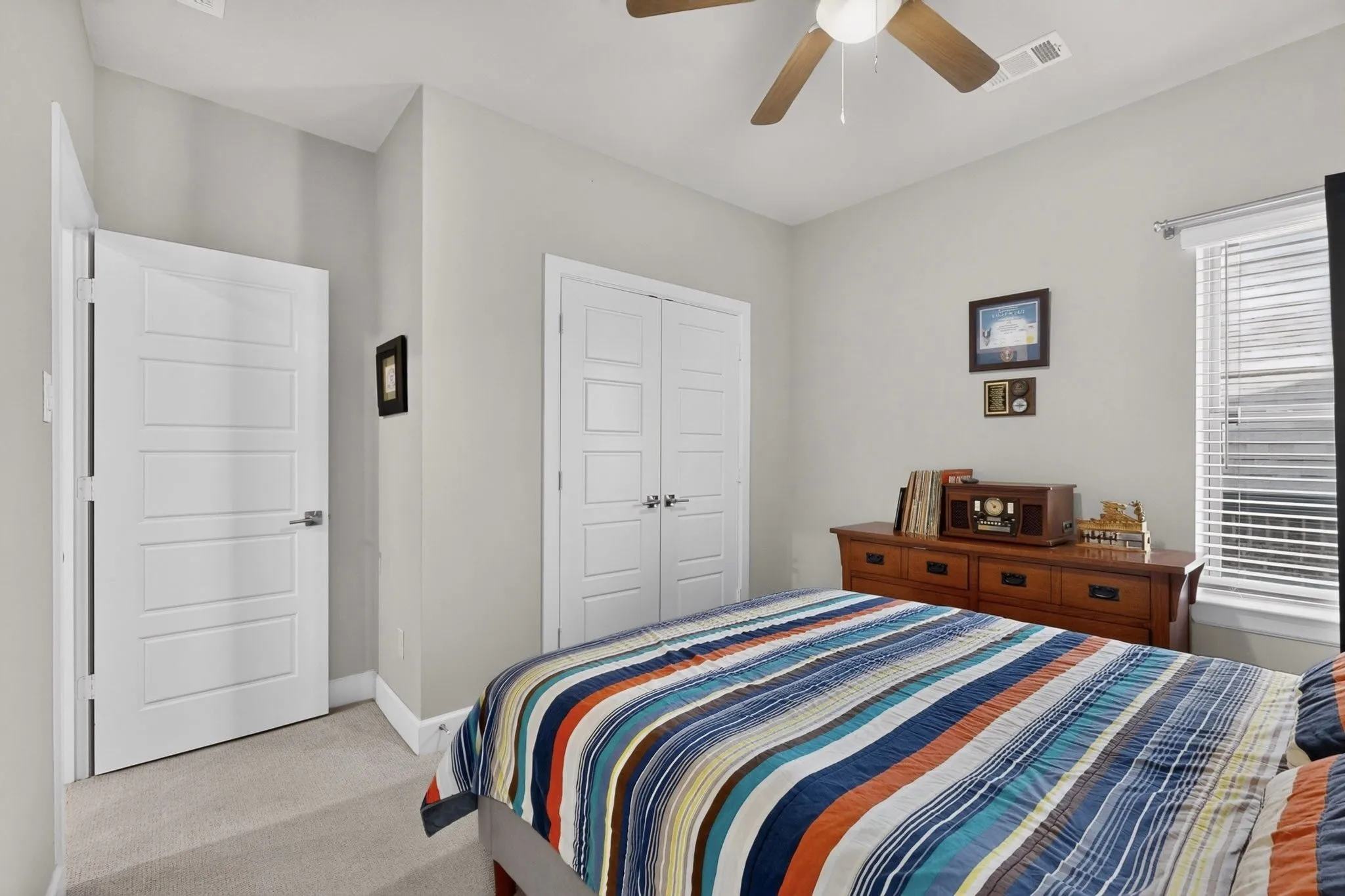 Carpeted room featuring a ceiling fan with integrated lighting, a window with blinds, and two panel doors