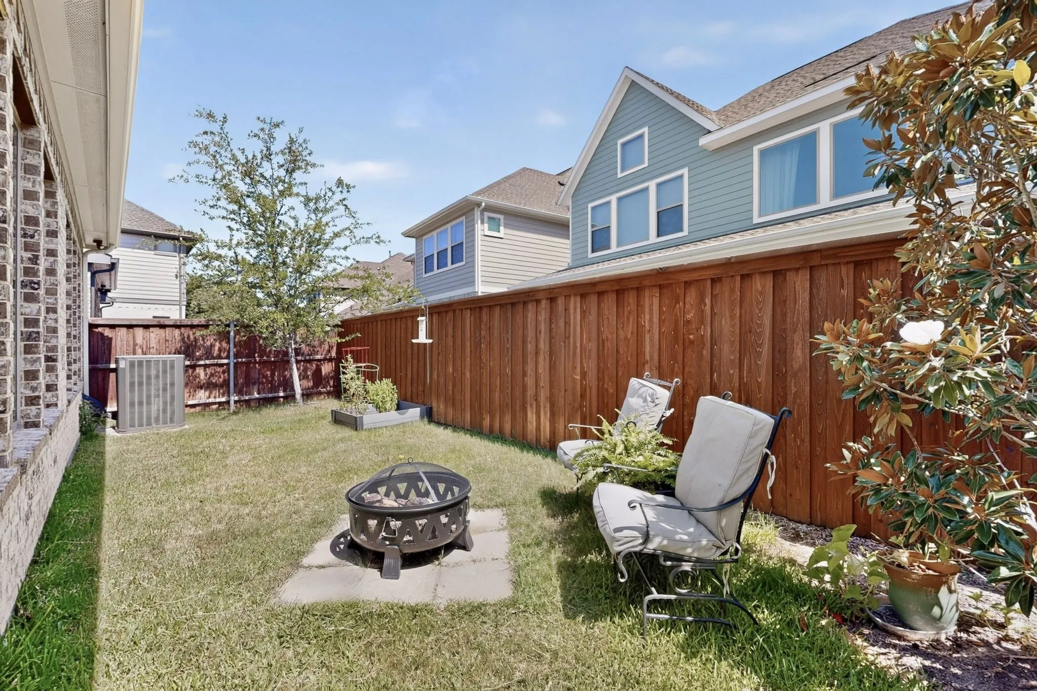 Fenced backyard with a fire pit on paver stones, featuring mature perimeter trees and brick siding on the home