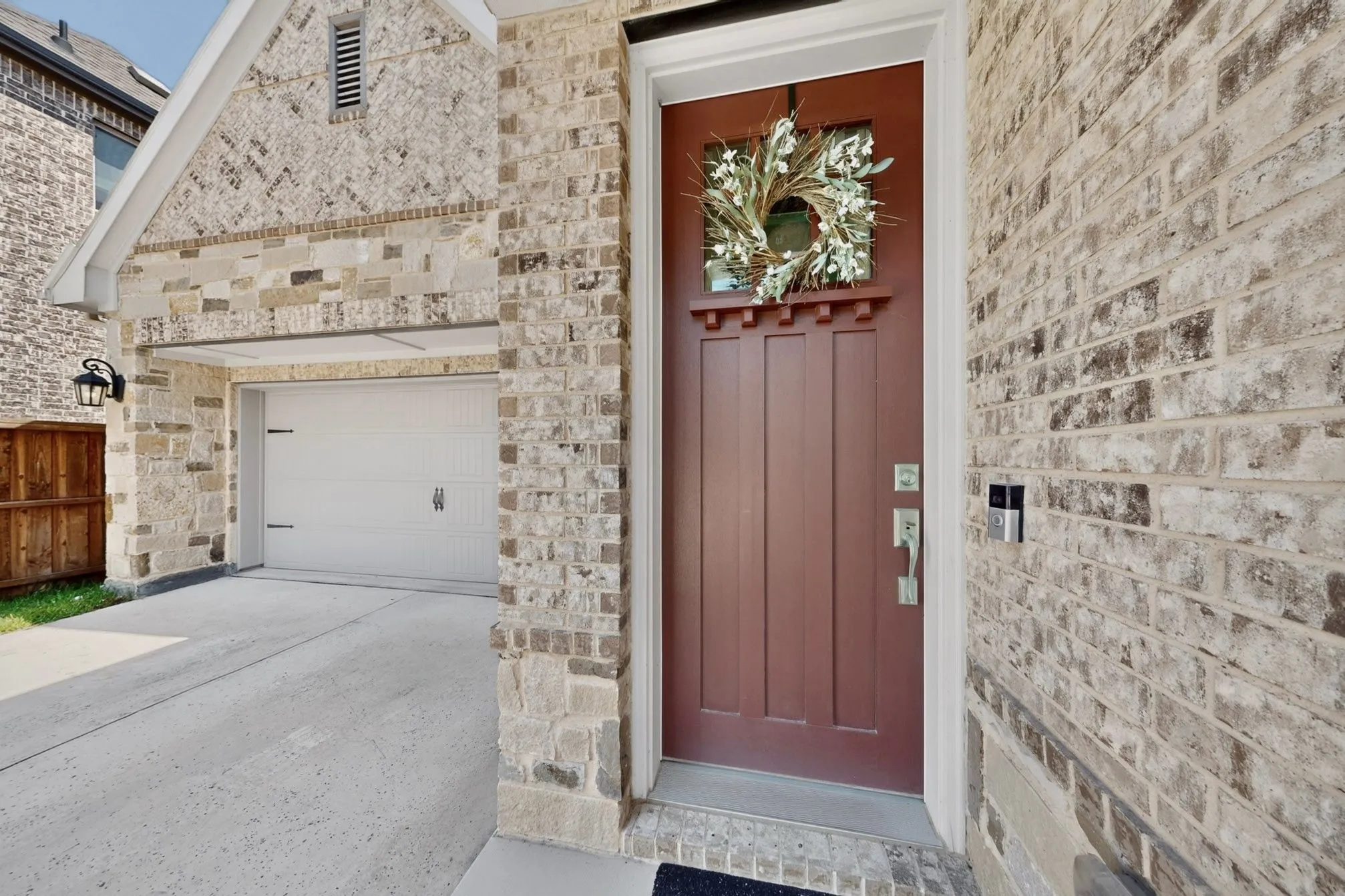 Architectural brick exterior featuring a warm-toned entry door with decorative glass, a concrete driveway, and an attached garage with a panel door