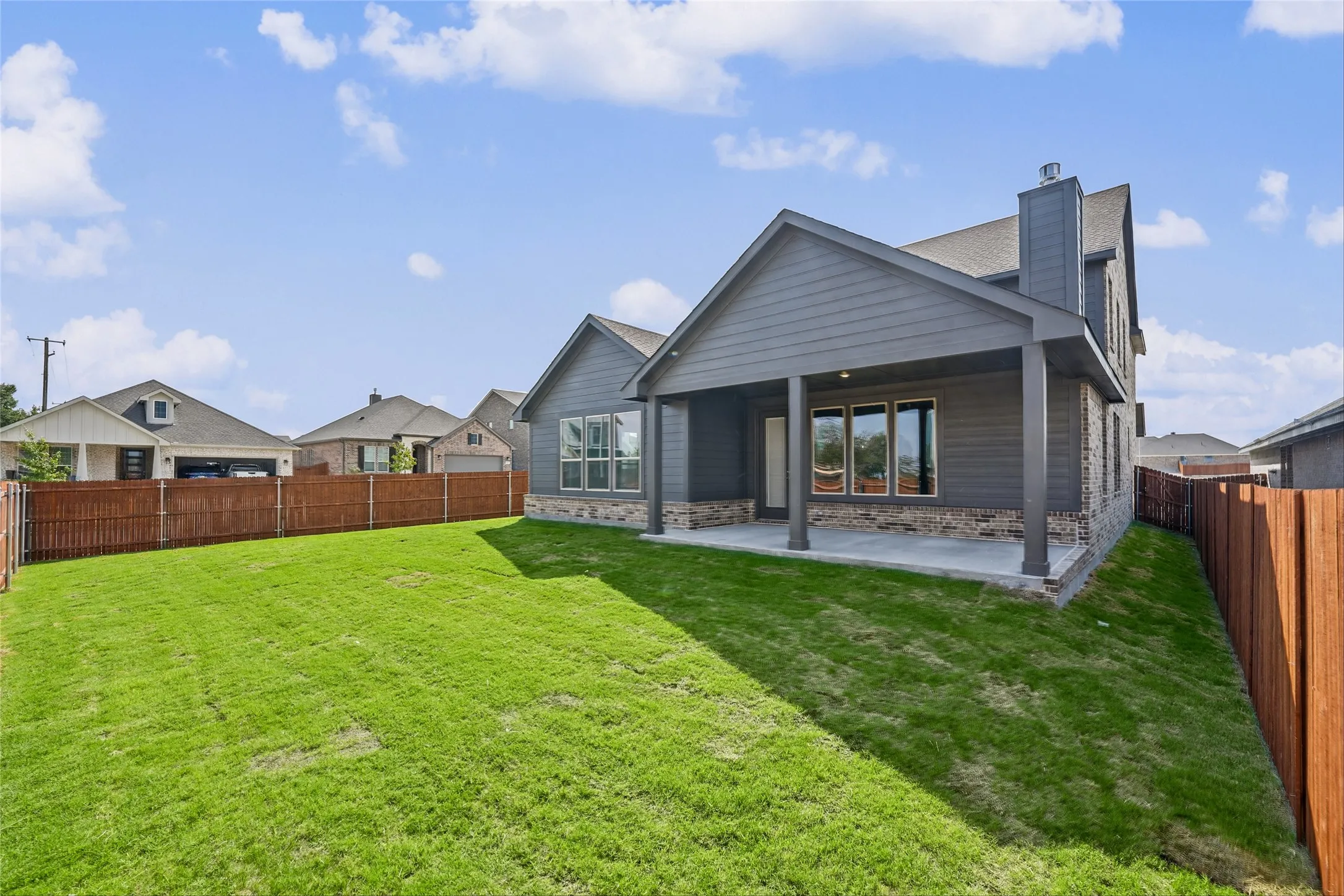 Expansive backyard featuring a covered patio, wood fencing, and a sloped lawn