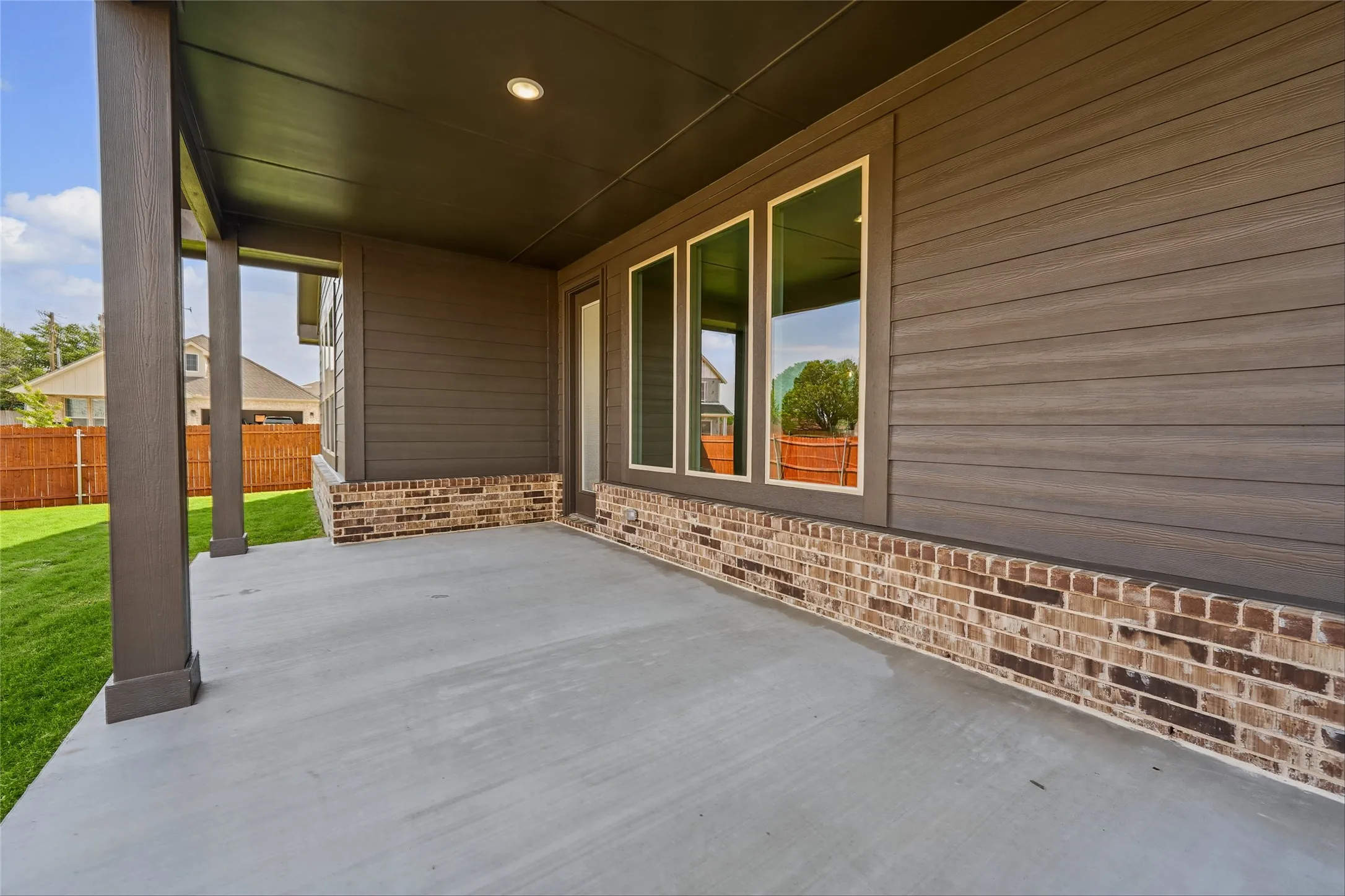Covered concrete patio with recessed lighting, supported by square columns, and a brick and horizontal siding exterior
