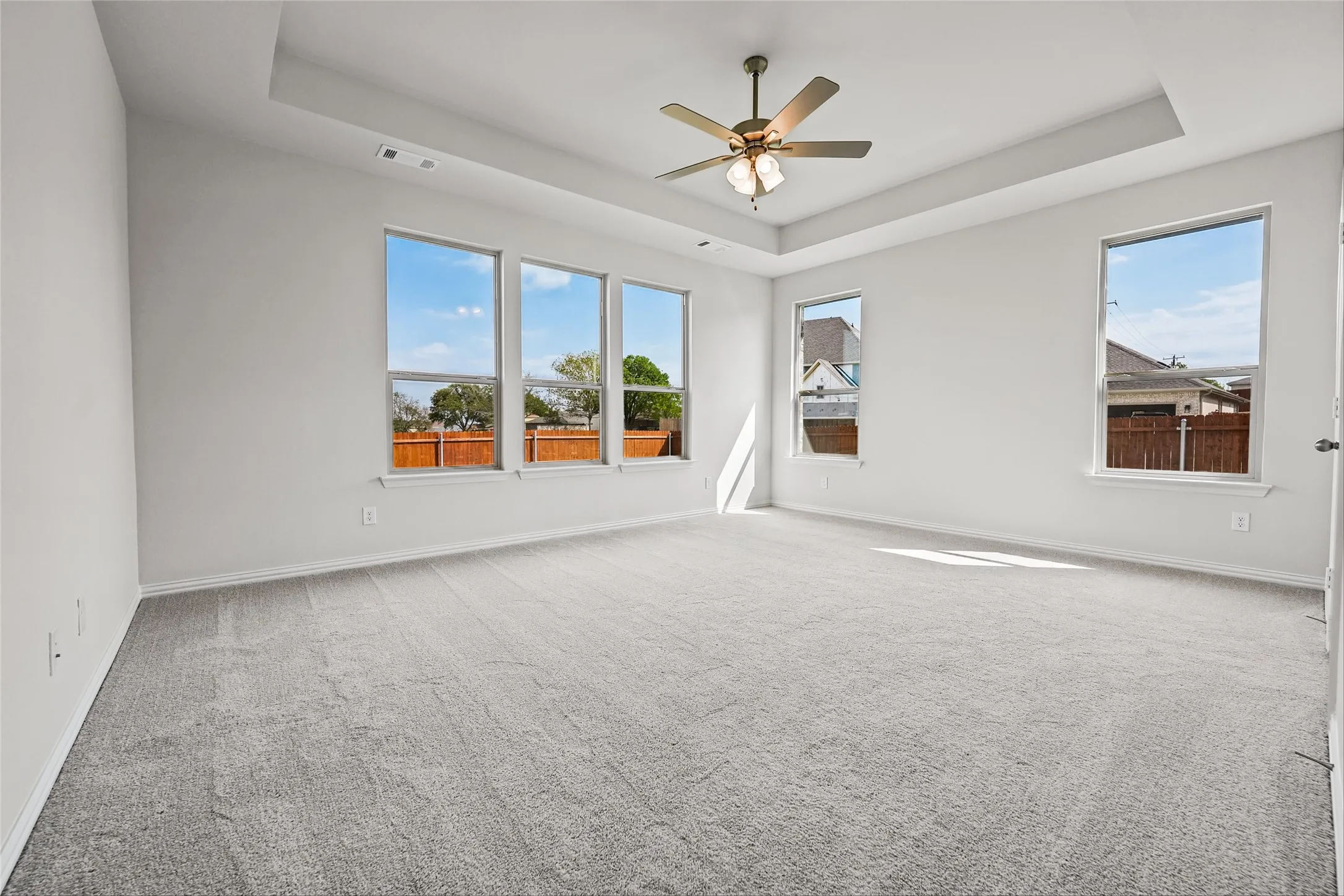 Spacious room featuring a tray ceiling, ceiling fan, and light gray carpeting