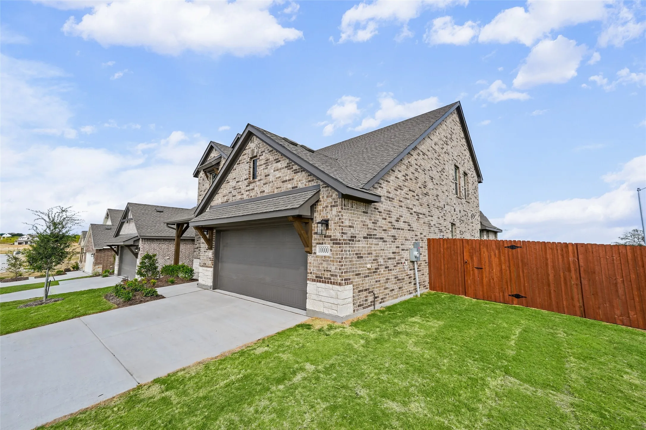 Brick exterior with stone accents, a concrete driveway, a wood fence, and a gray asphalt shingle roof