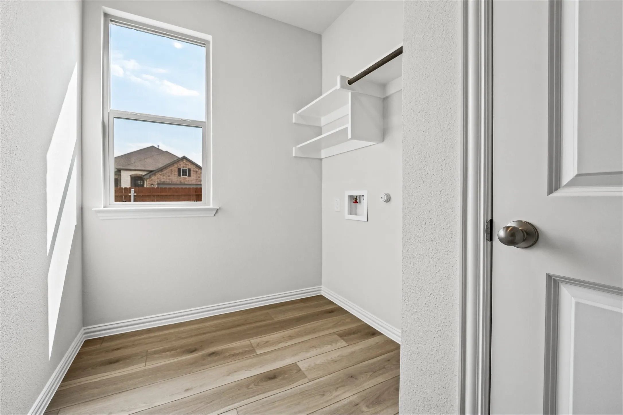 Utility area featuring wood-finish flooring, a single window, built-in shelving, and a hanging rod