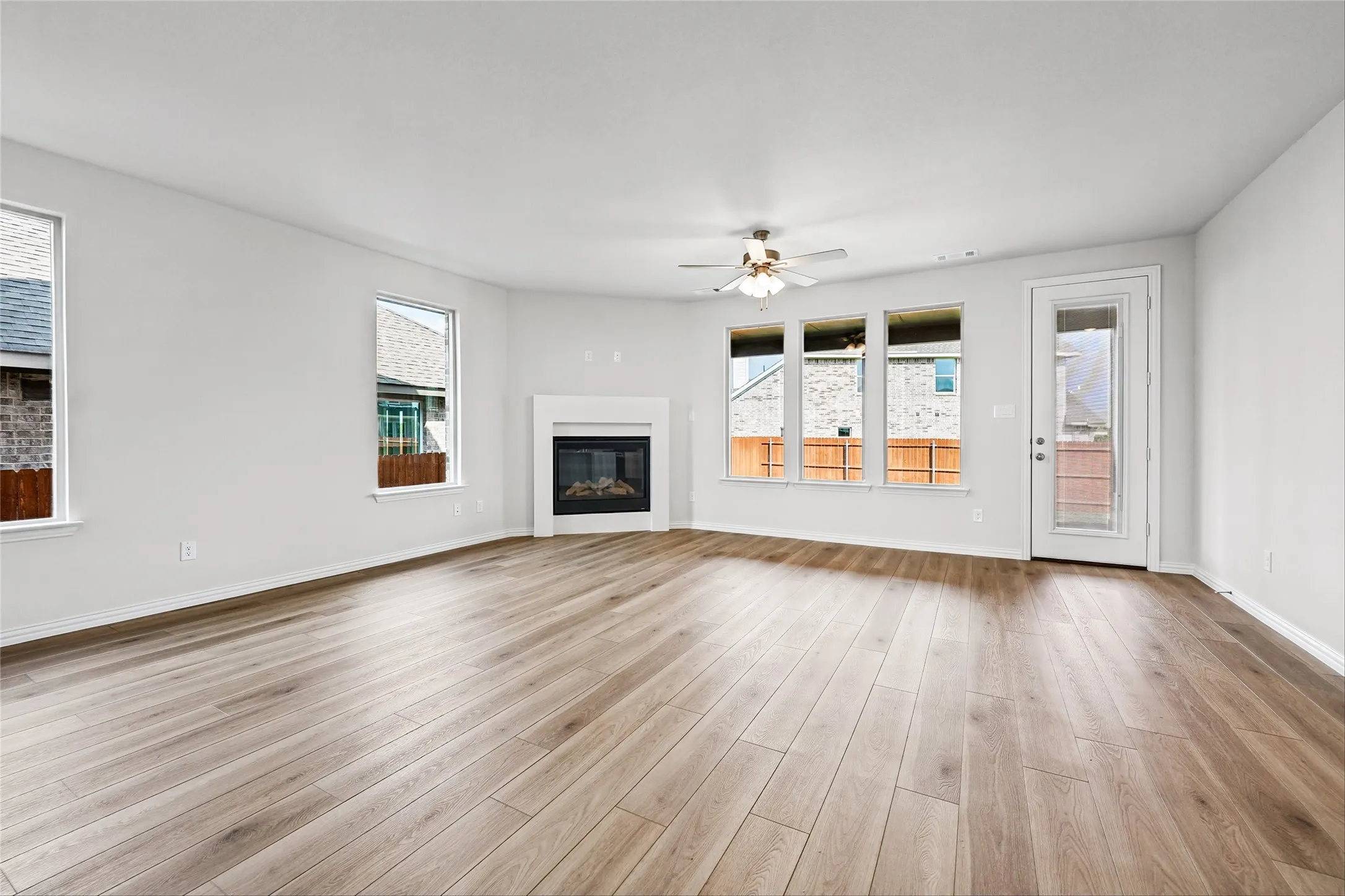 Expansive room featuring wood-finish flooring, multiple windows, a ceiling fan, and a built-in fireplace with a mantel