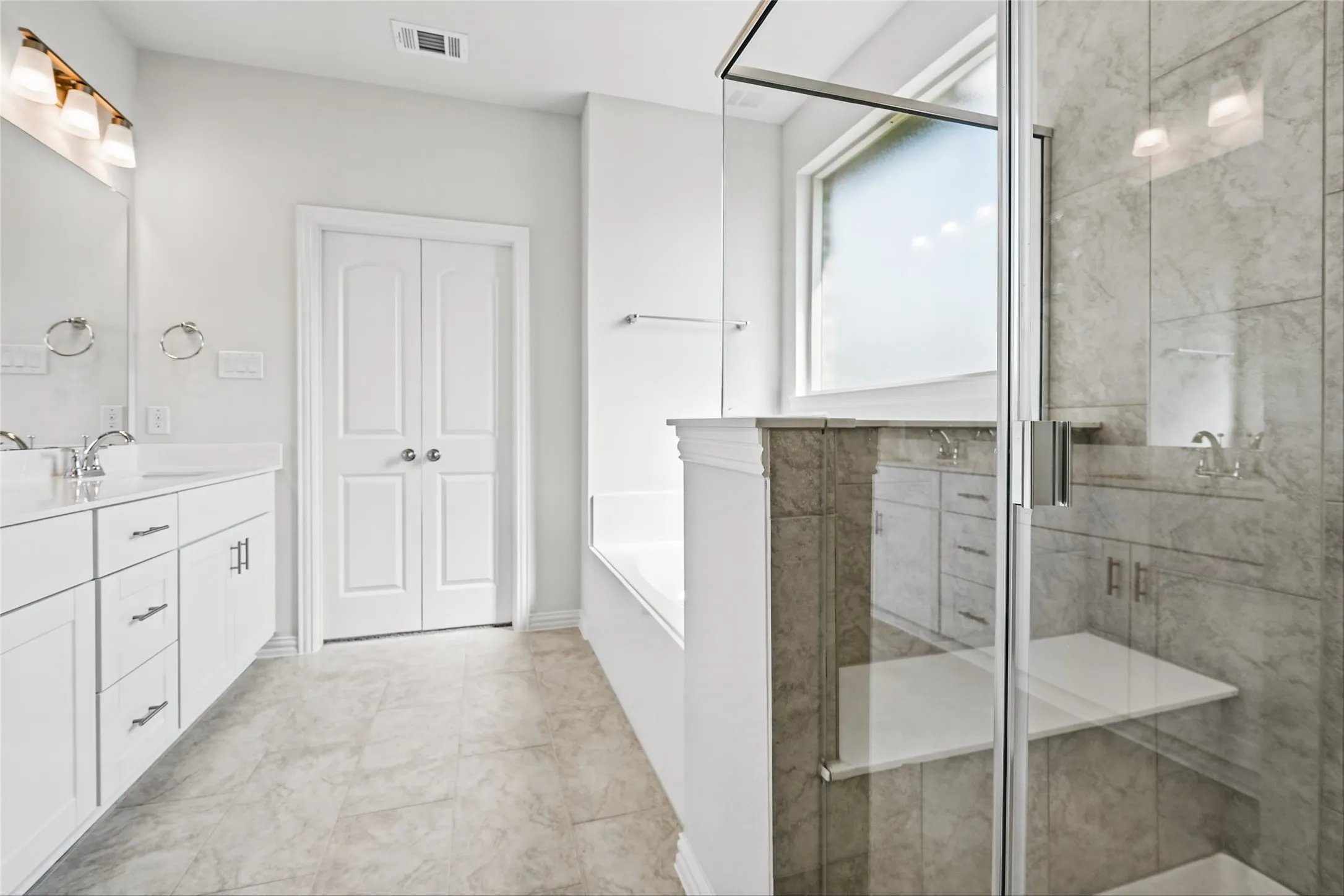 Dual vanity with undermount sinks, frameless glass shower enclosure, built-in shower shelving, large soaking tub, and frosted window