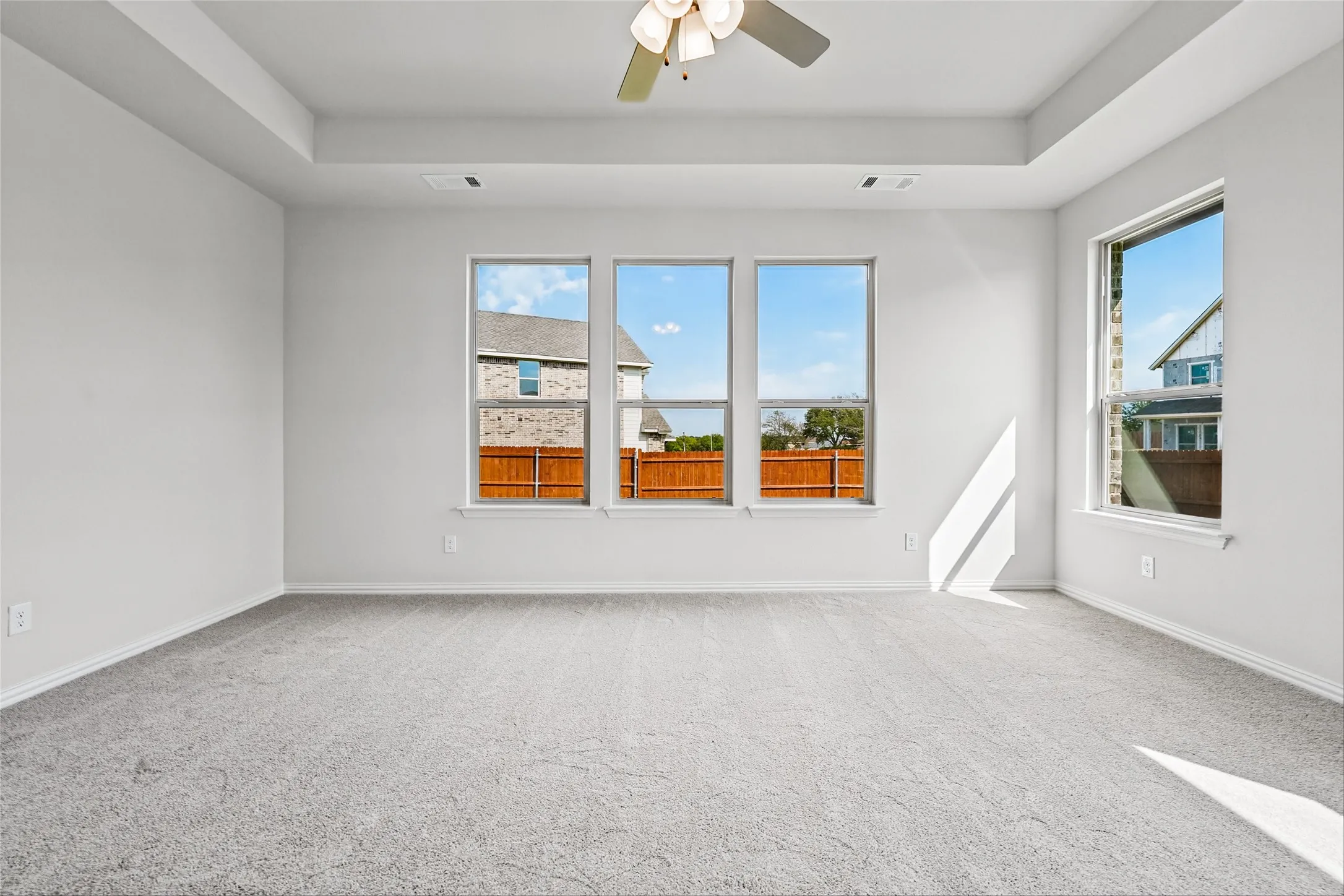 Recessed ceiling featuring a ceiling fan, light gray carpeting, and multiple windows
